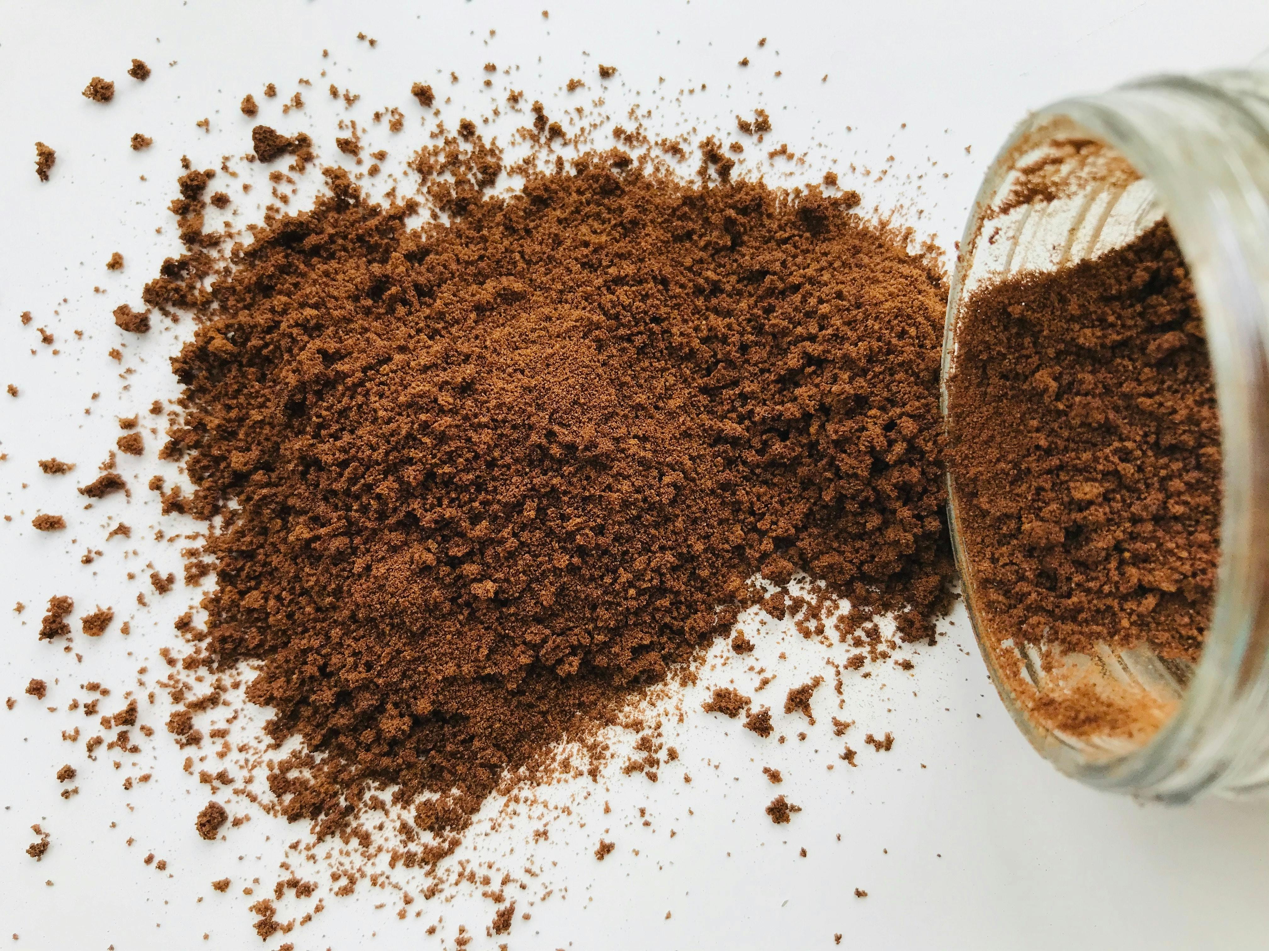 An open container spills some coffee grounds out on to a table.