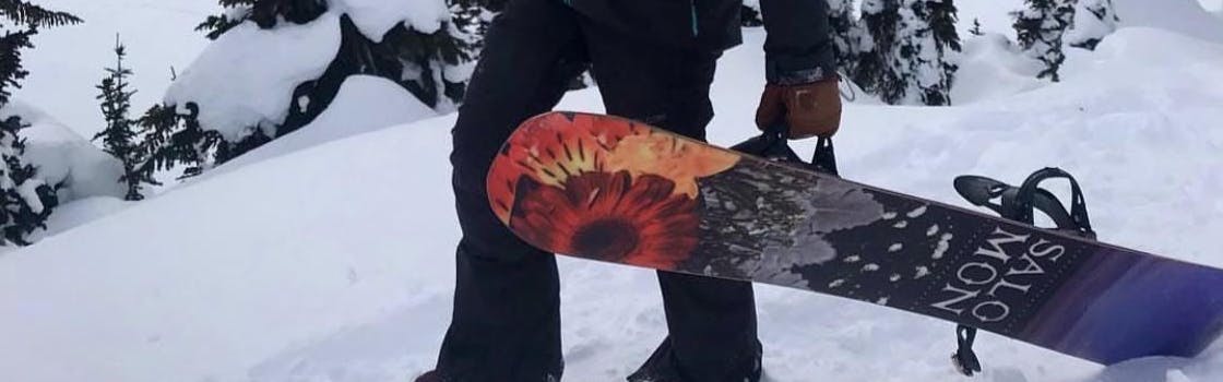 A snowboarder standing with the Salomon Gypsy snowboard. 