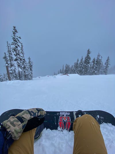 Top down view of a snowboard as the rider is sitting in the snow at the top of a snowy run. 