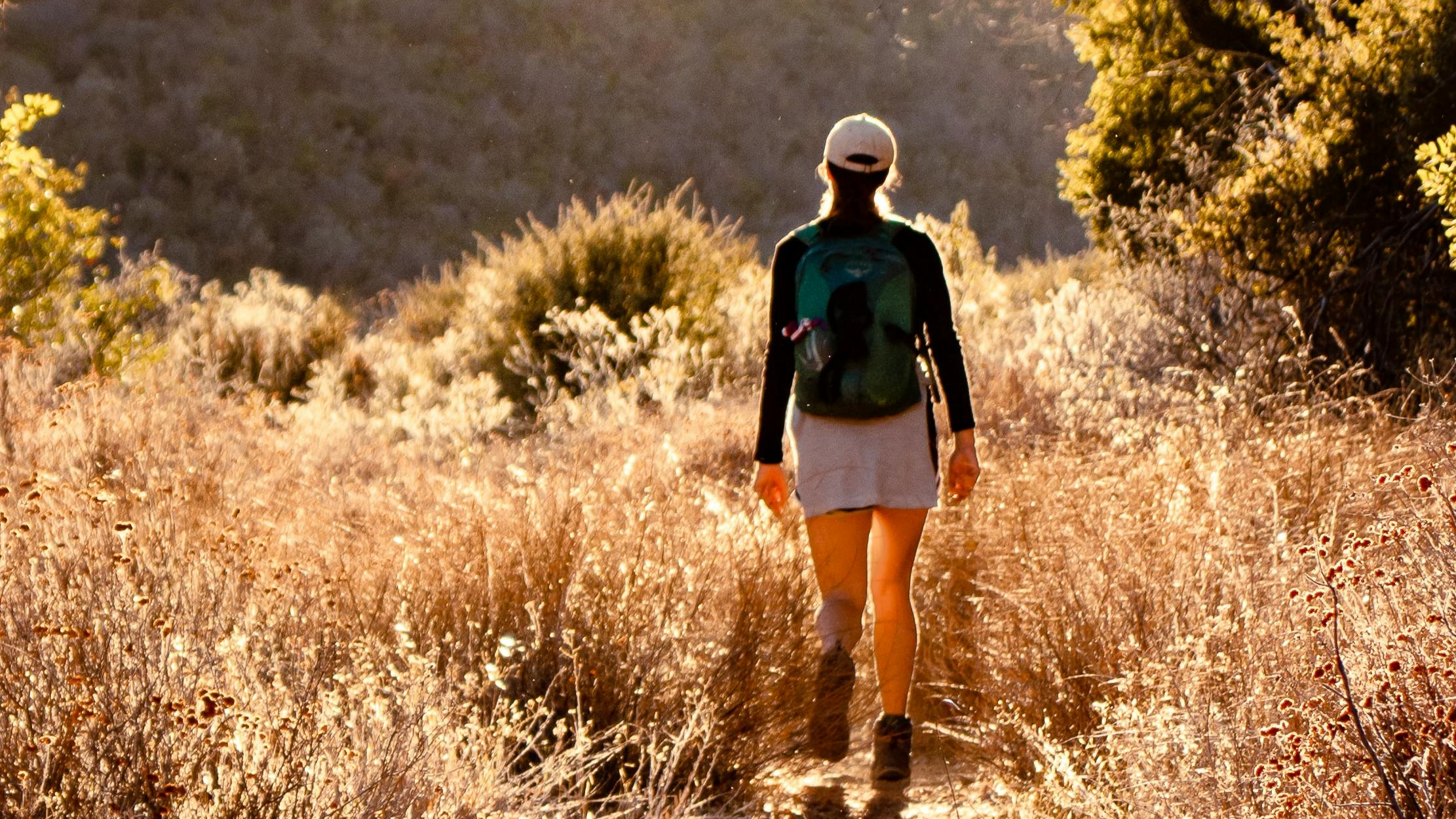 A woman walks on a grassy trail. 