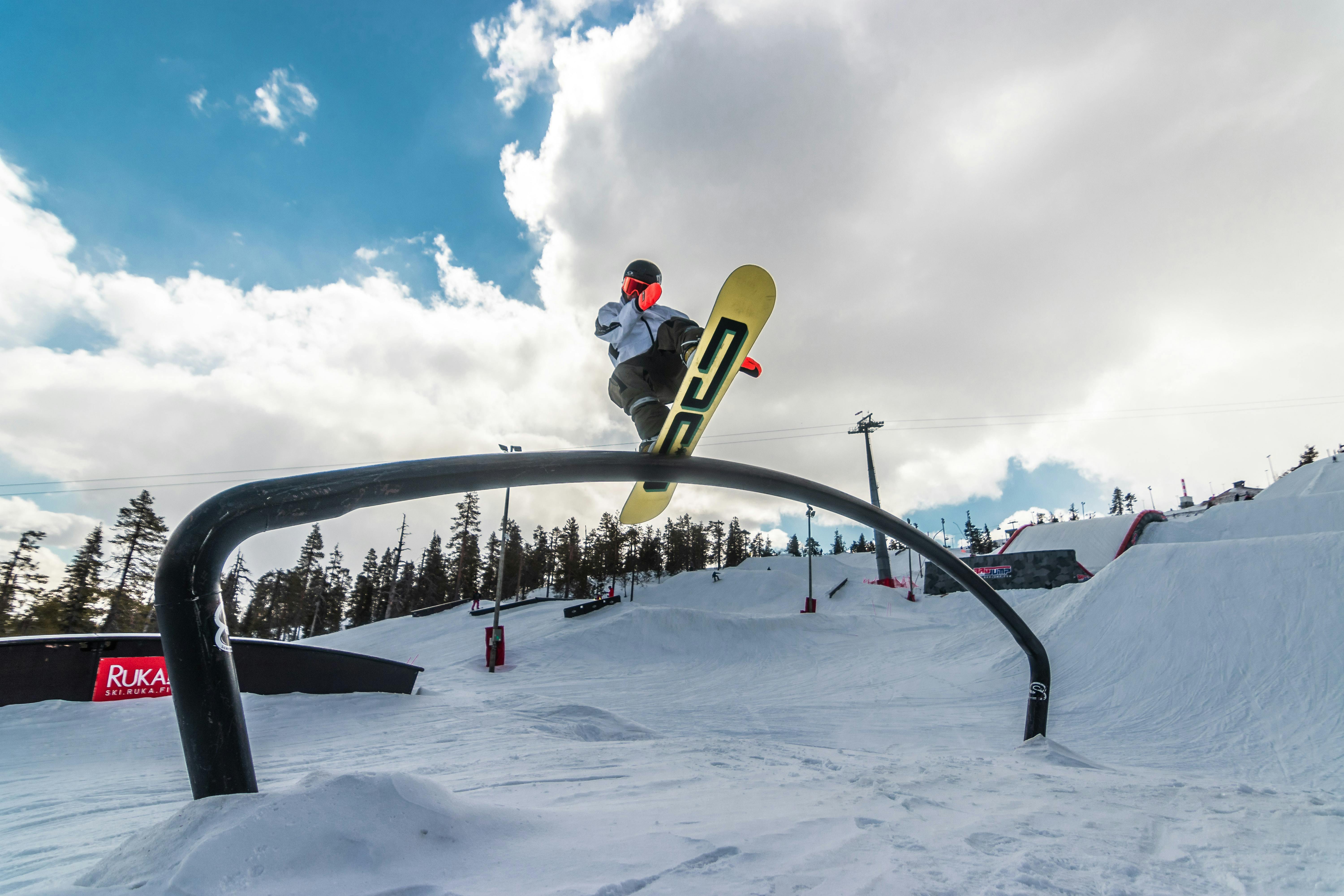 A snowboarder does a slide across a rail in a terrain park. His board is yellow and it is sunny.