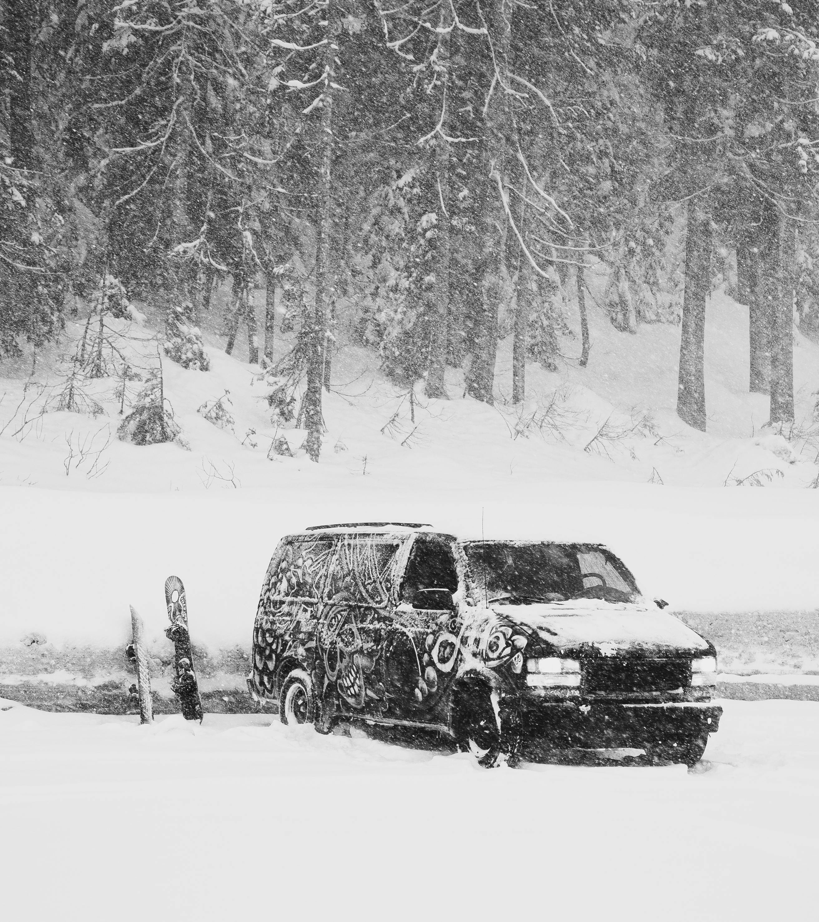 A van is parked in a snowy area with a snowboard next to it.