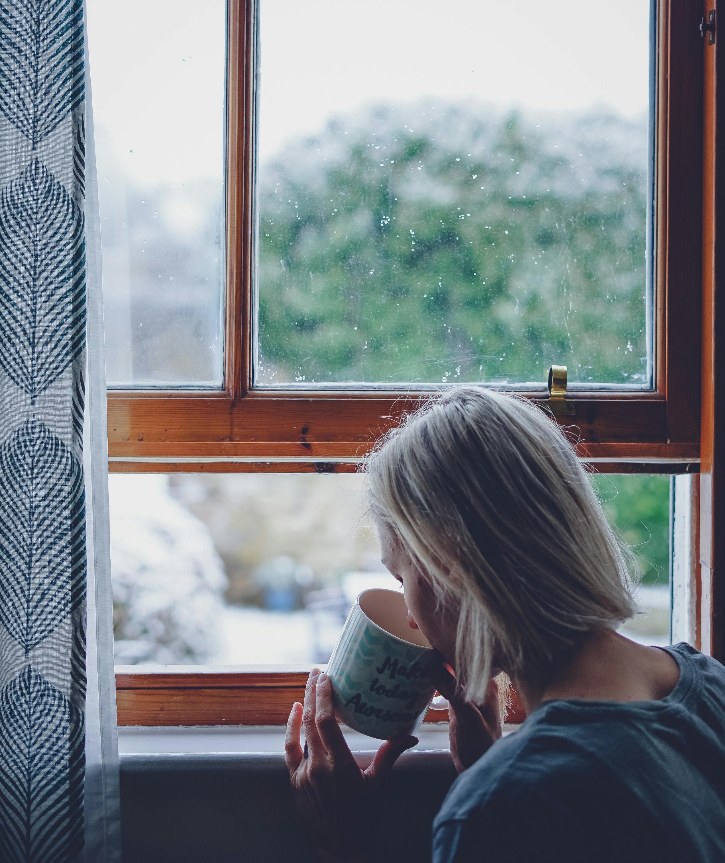 A woman drinks a cup of coffee by an open window. 