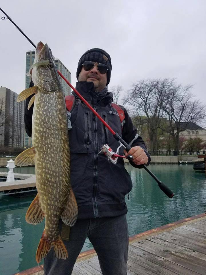 The author stands on a dock and holds up a large Great Lakes Pike.
