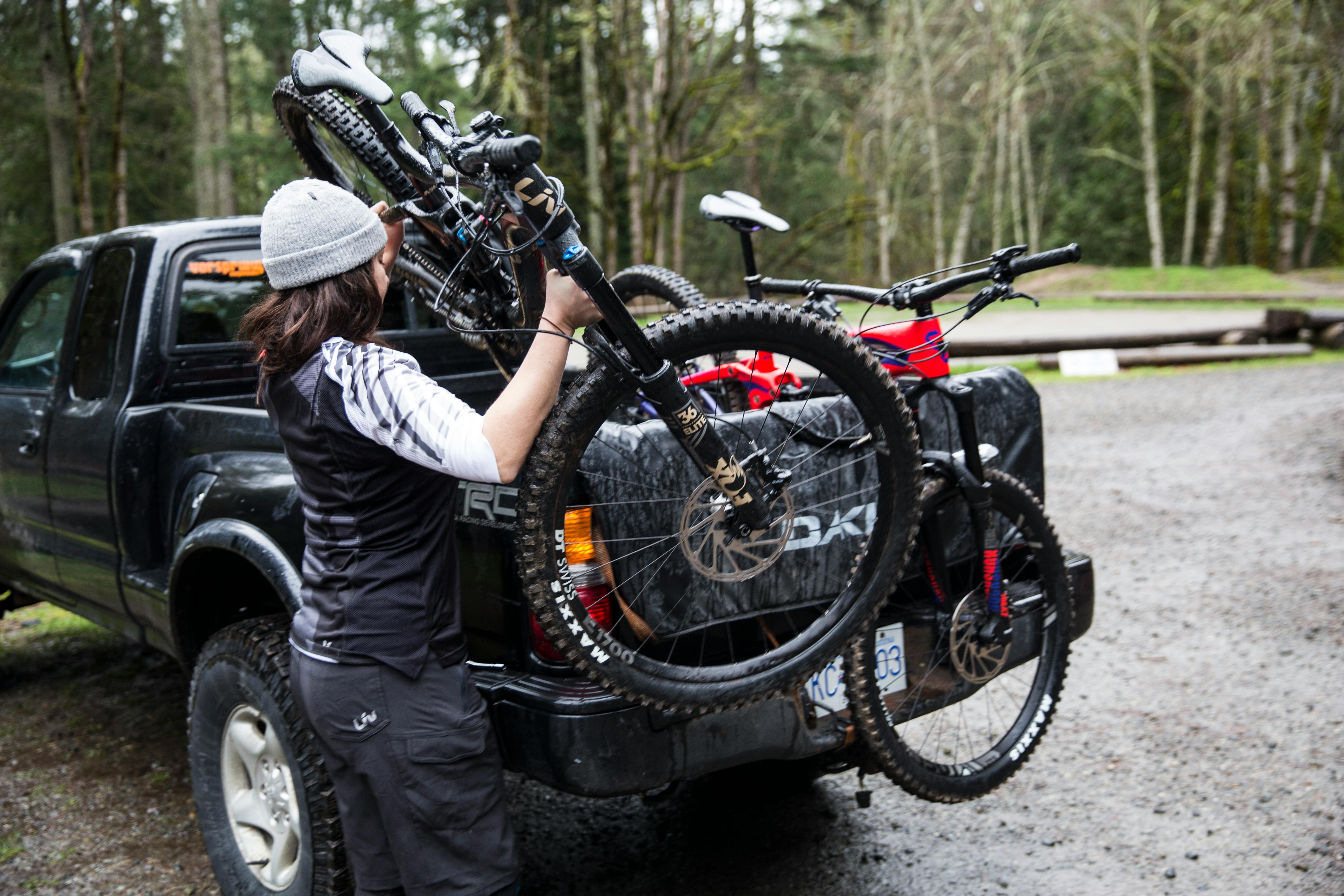 A woman loading mountain bikes into the back of a black pickup truck.