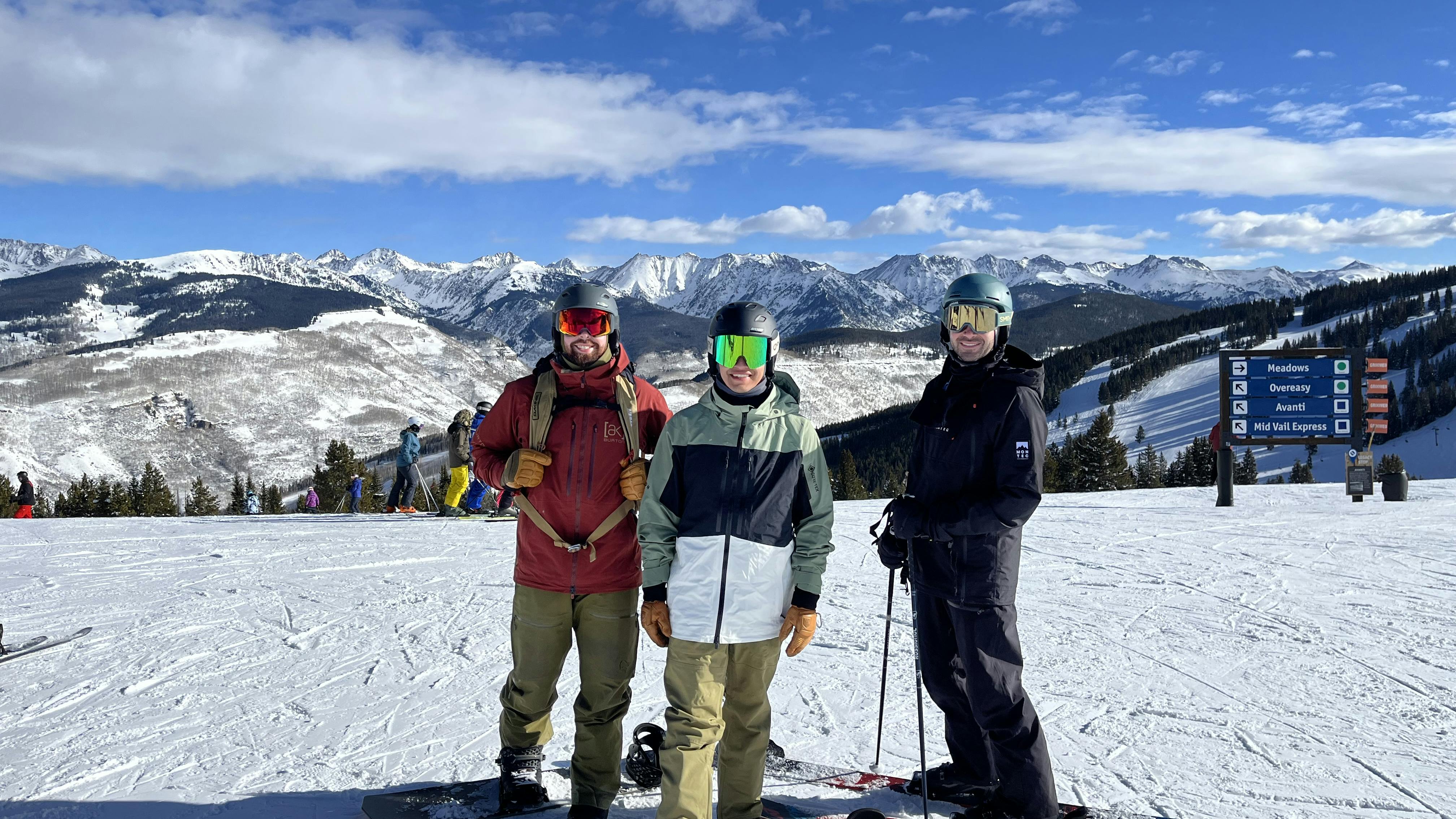Two snowboarders and a skier pose at the top of a sunny ski run. One is wearing the Burton Men's GORE-TEX® Swash Insulated Jacket. 