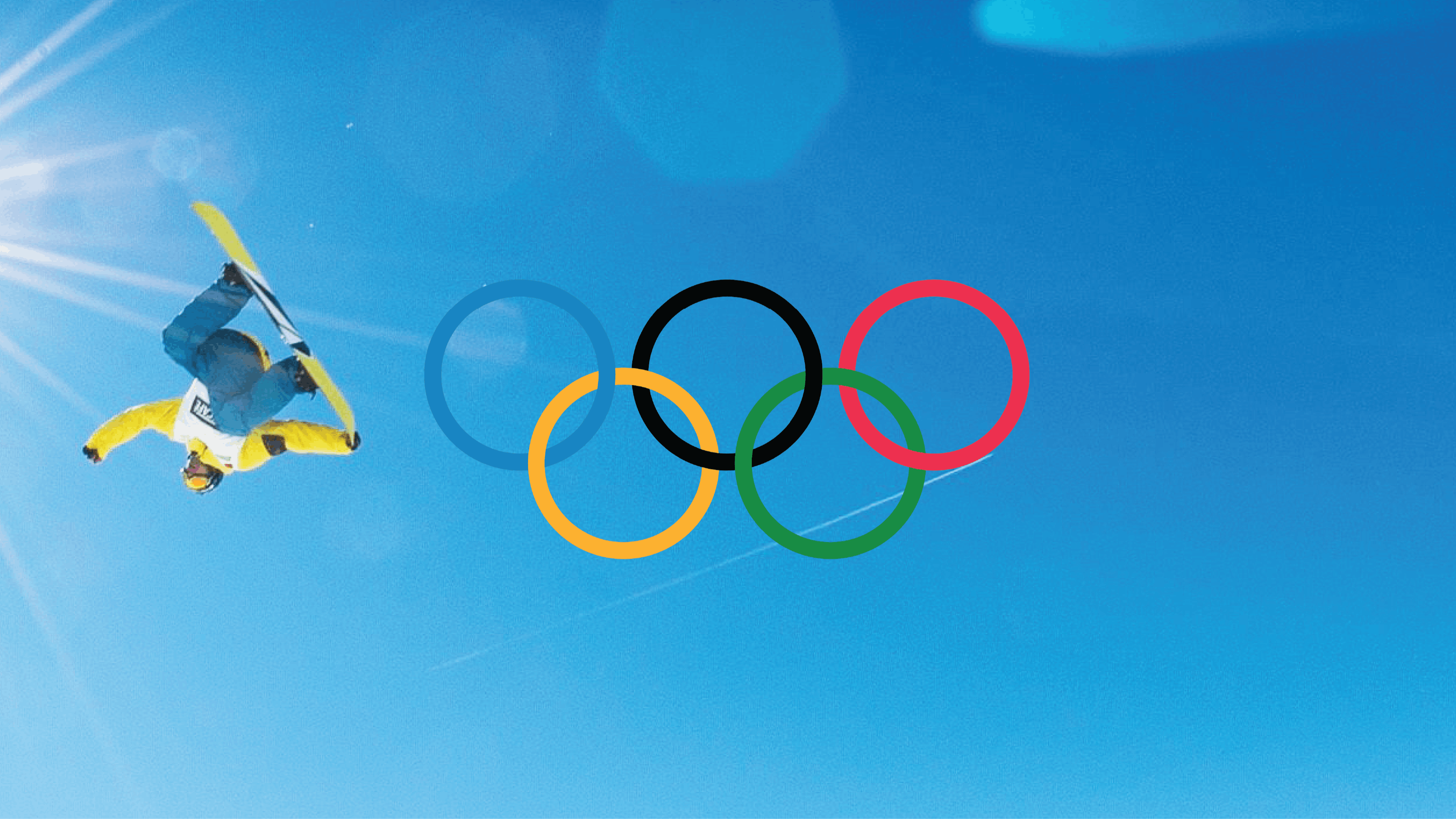 A snowboarder jumps upside down and grabs his board on a blue-sky, sunny day. The Olympic rings are added on top. 