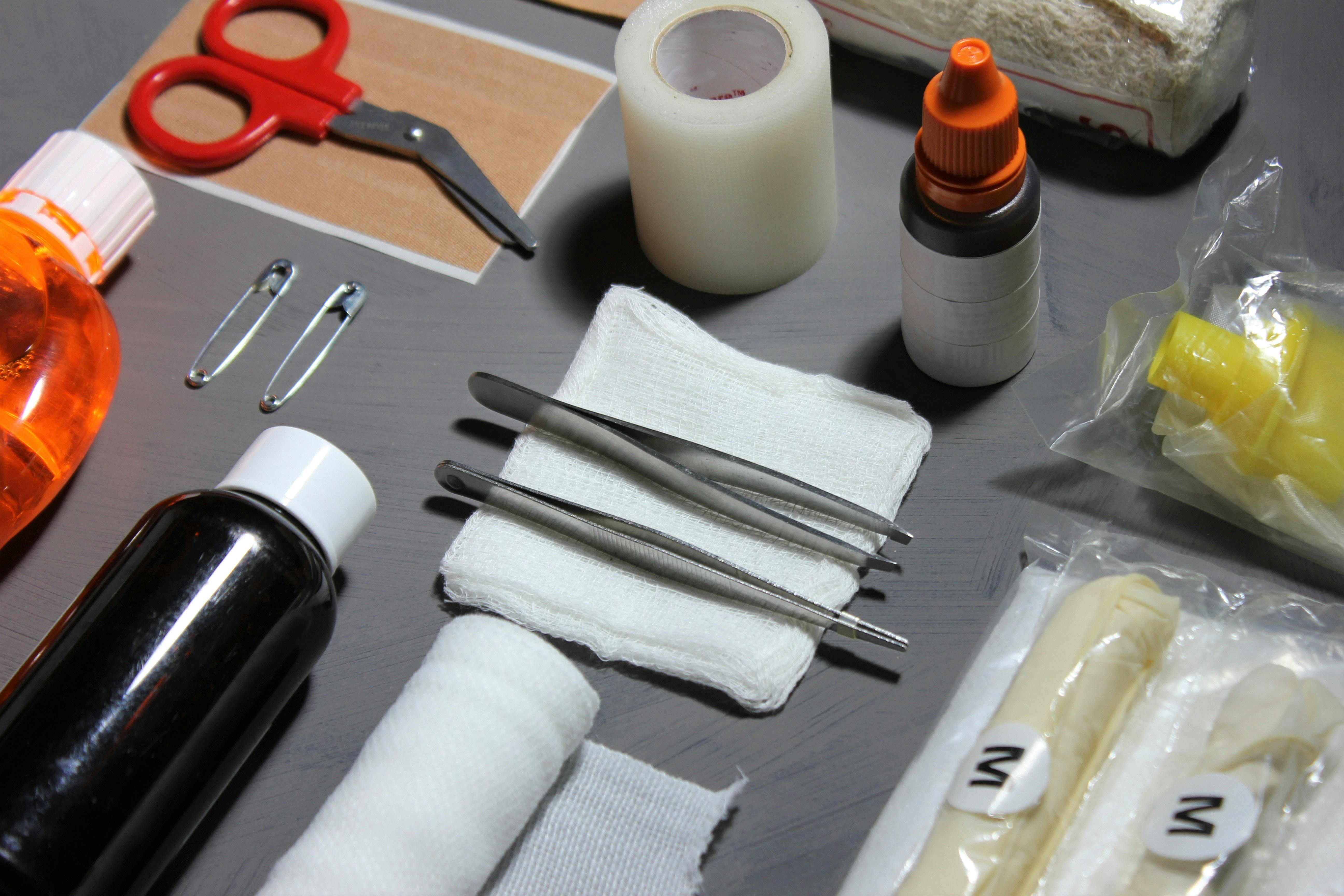 The contents of a first aid kit laid out on a table, including tweezers, tape, scissors, and gauze.
