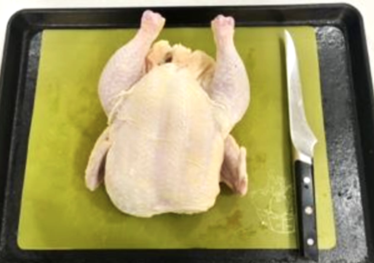 A raw chicken sitting on a cutting board next to a knife. 