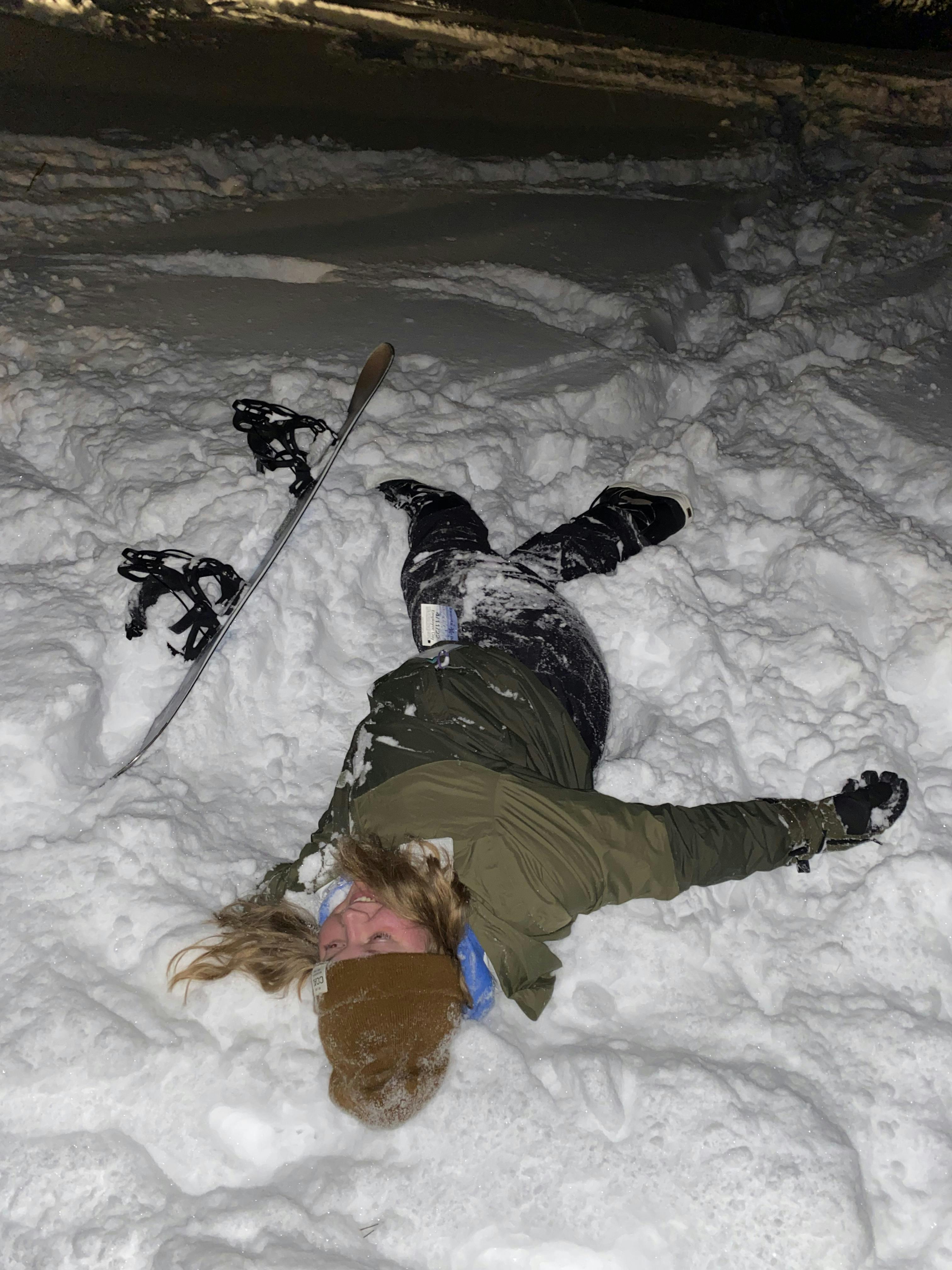 A snowboarder laying in the snow next to her snowboard. 