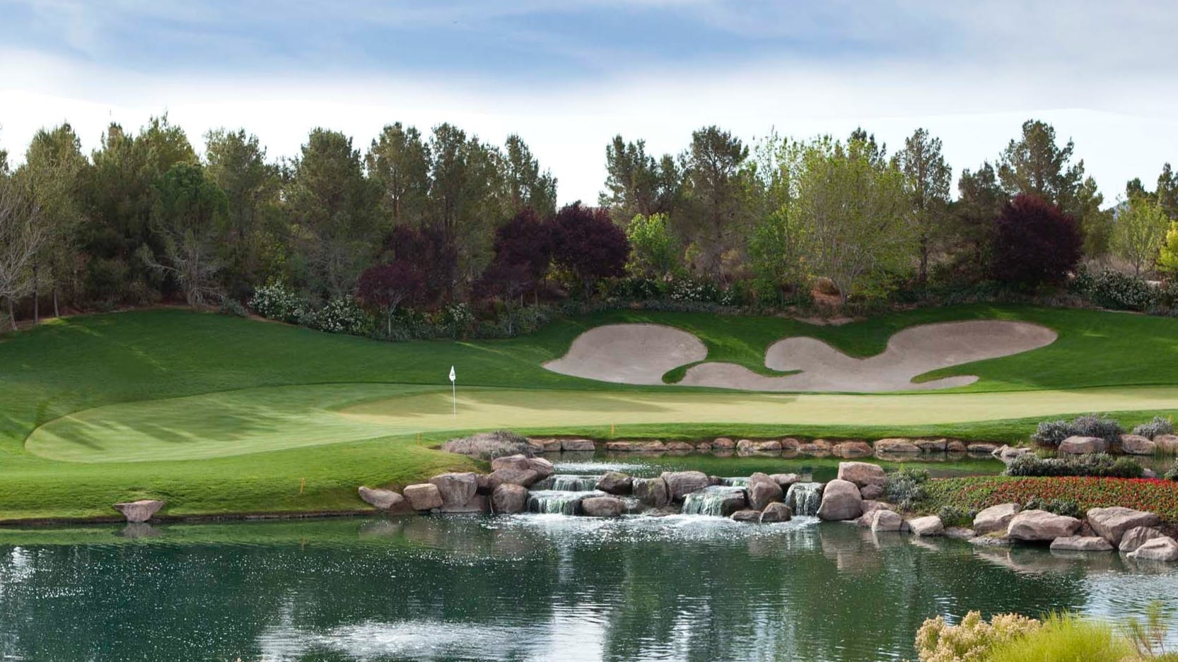 A landscape of a lush golf course with a pond and sand traps.