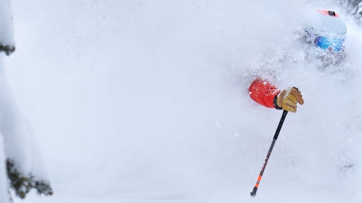 A man in ski gear is barely visible through the deep snow but you can make out a helmet and a gloved hand holding a ski pole.