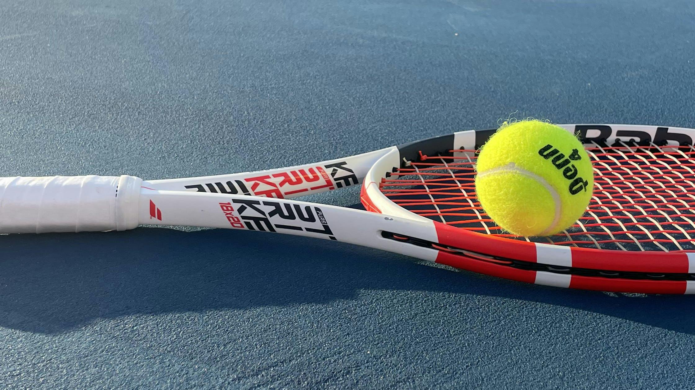 The Babolat Pure Strike 18x20 Racquet lying on a tennis court.