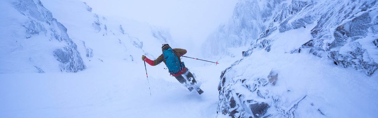 A skier turns down a narrow chute with his backpack and skis on.