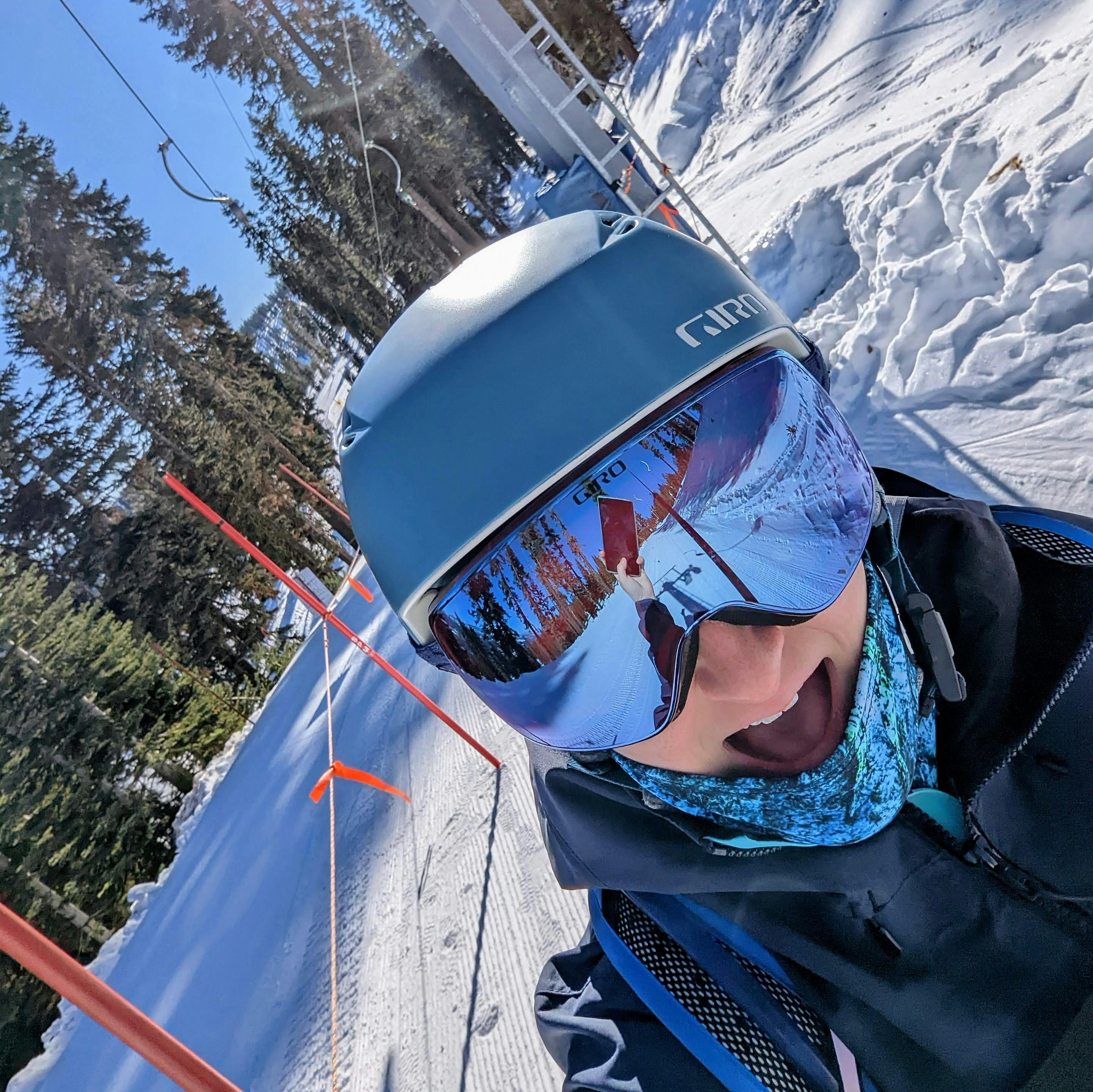 A skier wearing a blue Giro helmet. There is a ski run in the background. 