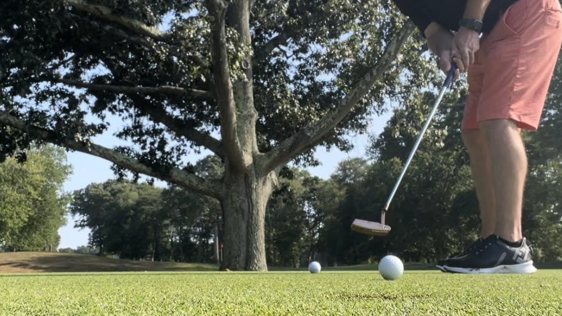 A man putts a golf ball on a course.