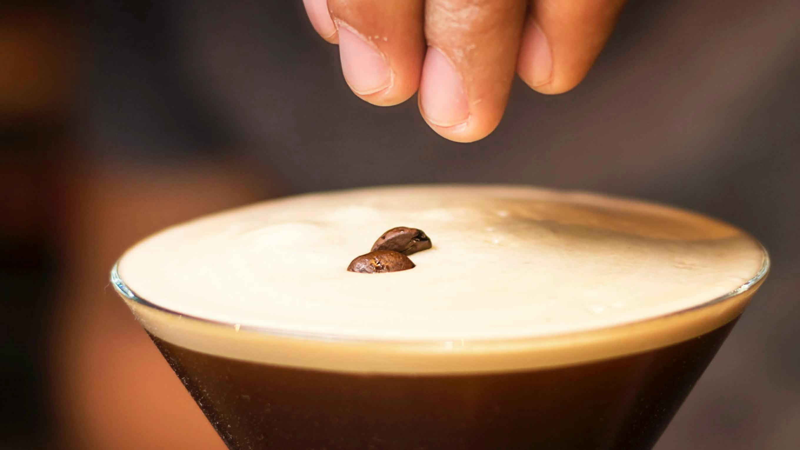 A bartender garnishes a finely poured Espresso Martini with coffee beans for a traditional yet sophisticated presentation.