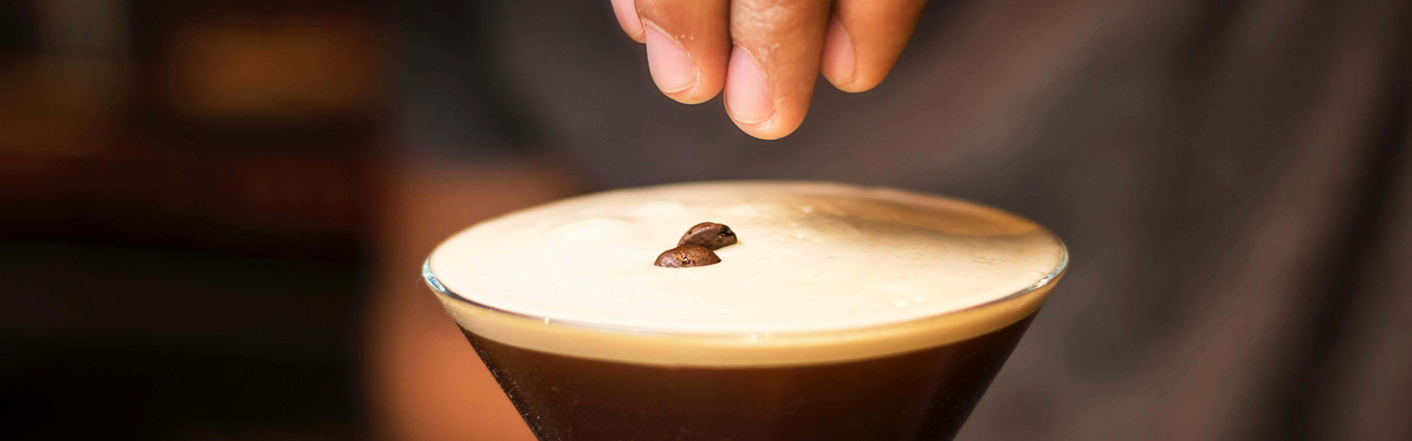 A bartender garnishes a finely poured Espresso Martini with coffee beans for a traditional yet sophisticated presentation.