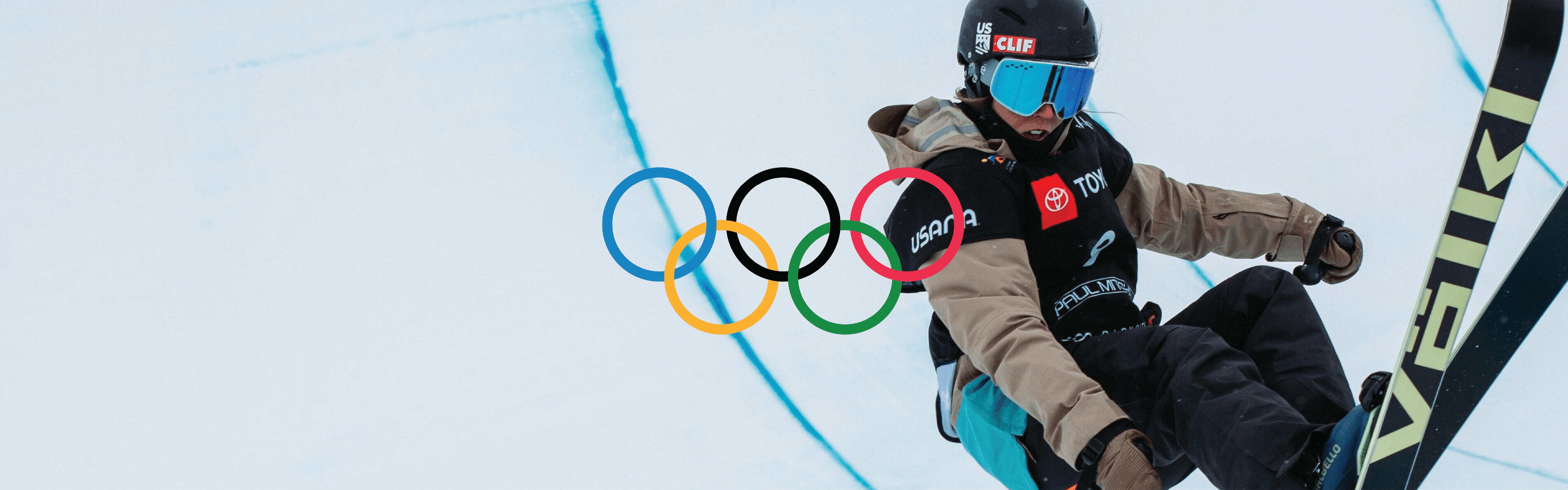 A skier comes out of the half-pipe with their Volkl skis. The Olympic rings are added on top of the image.