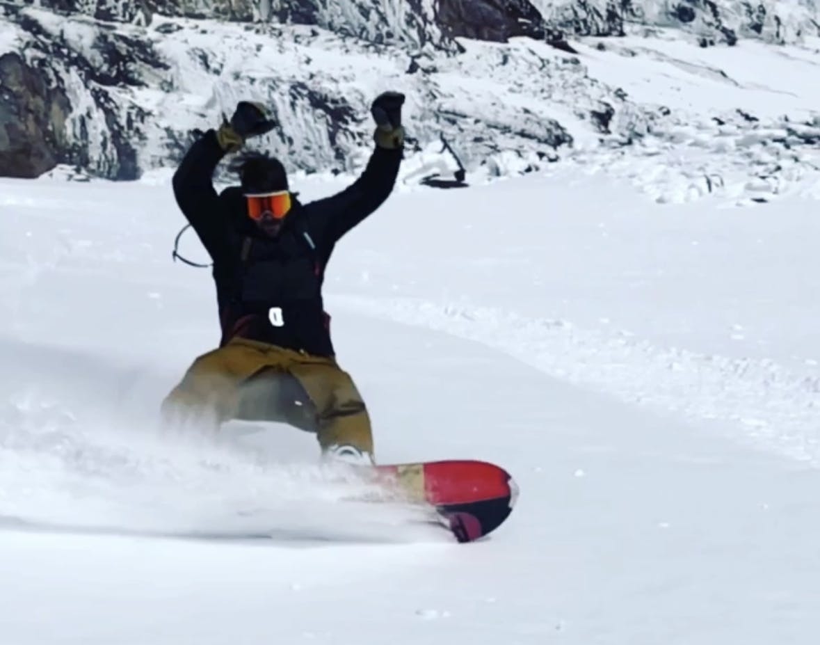 A snowboarder turning with his hands in the air.