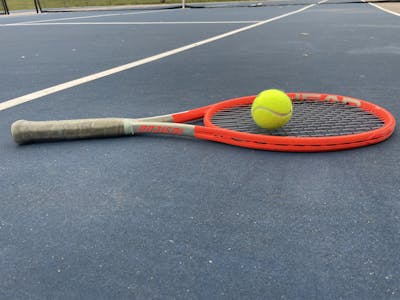 The Head Radical MP Tennis Racquet laying on a court with a ball on top of it. 