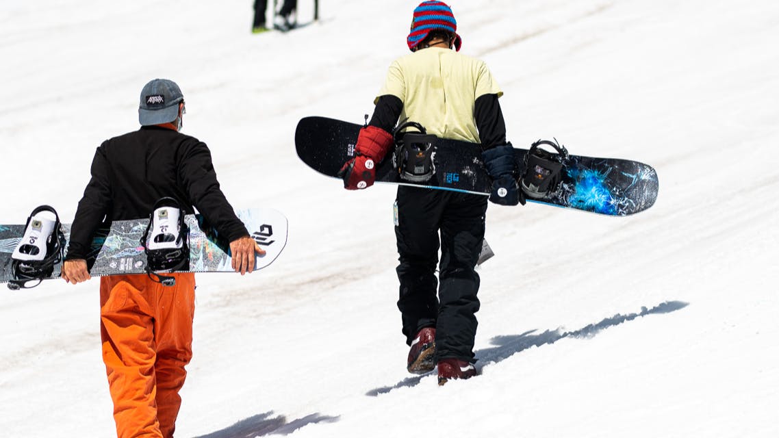 Two snowboarders walking up a slope carrying their boards