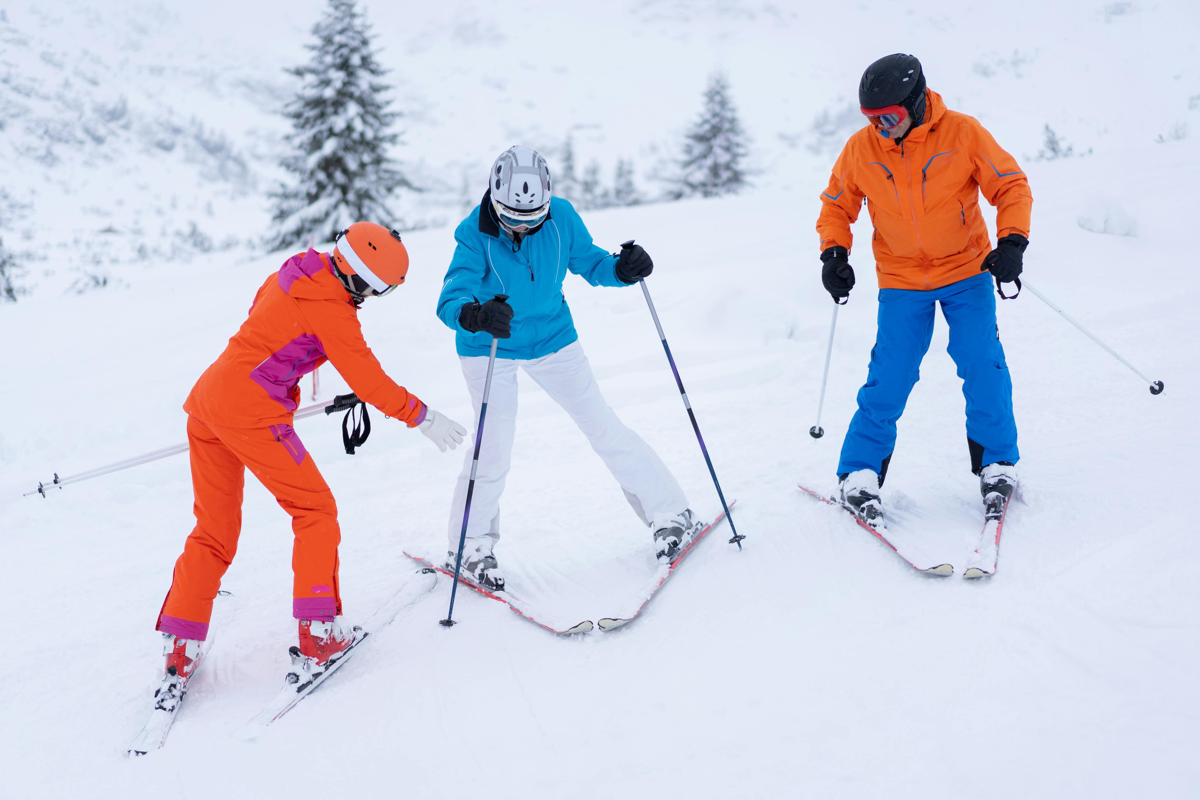 A woman instructs another woman how to position her skis while a man looks on