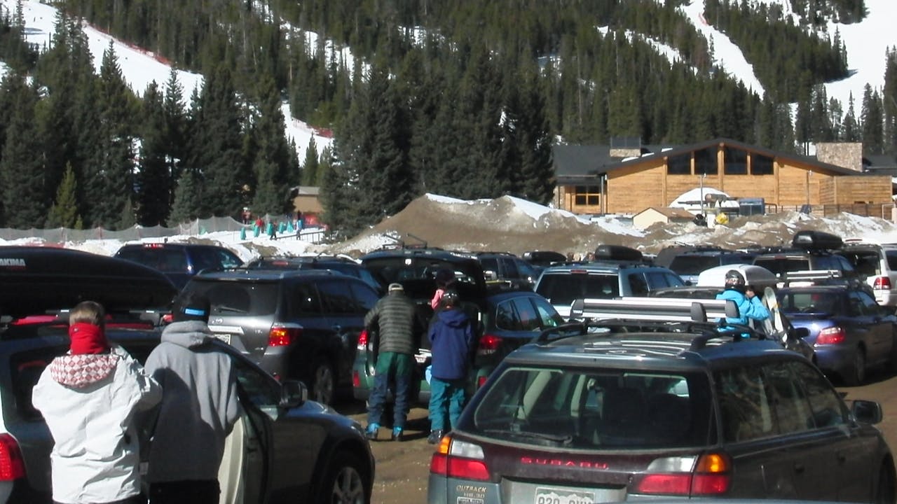 Several skiers getting ready for skiing in the parking lot of a ski resort. 