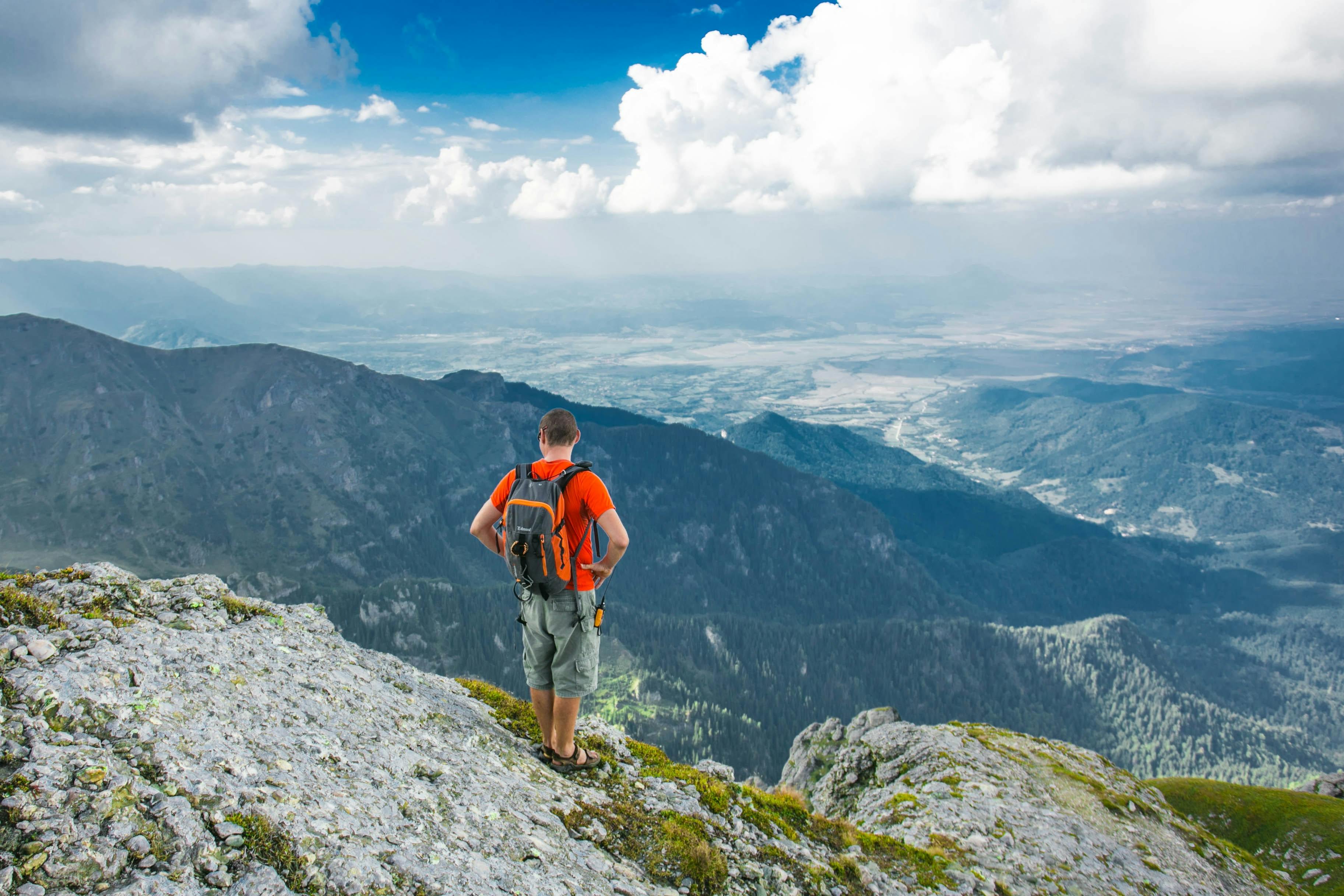 A man with a daypack on stares at the view at an overlook in the mountains. 