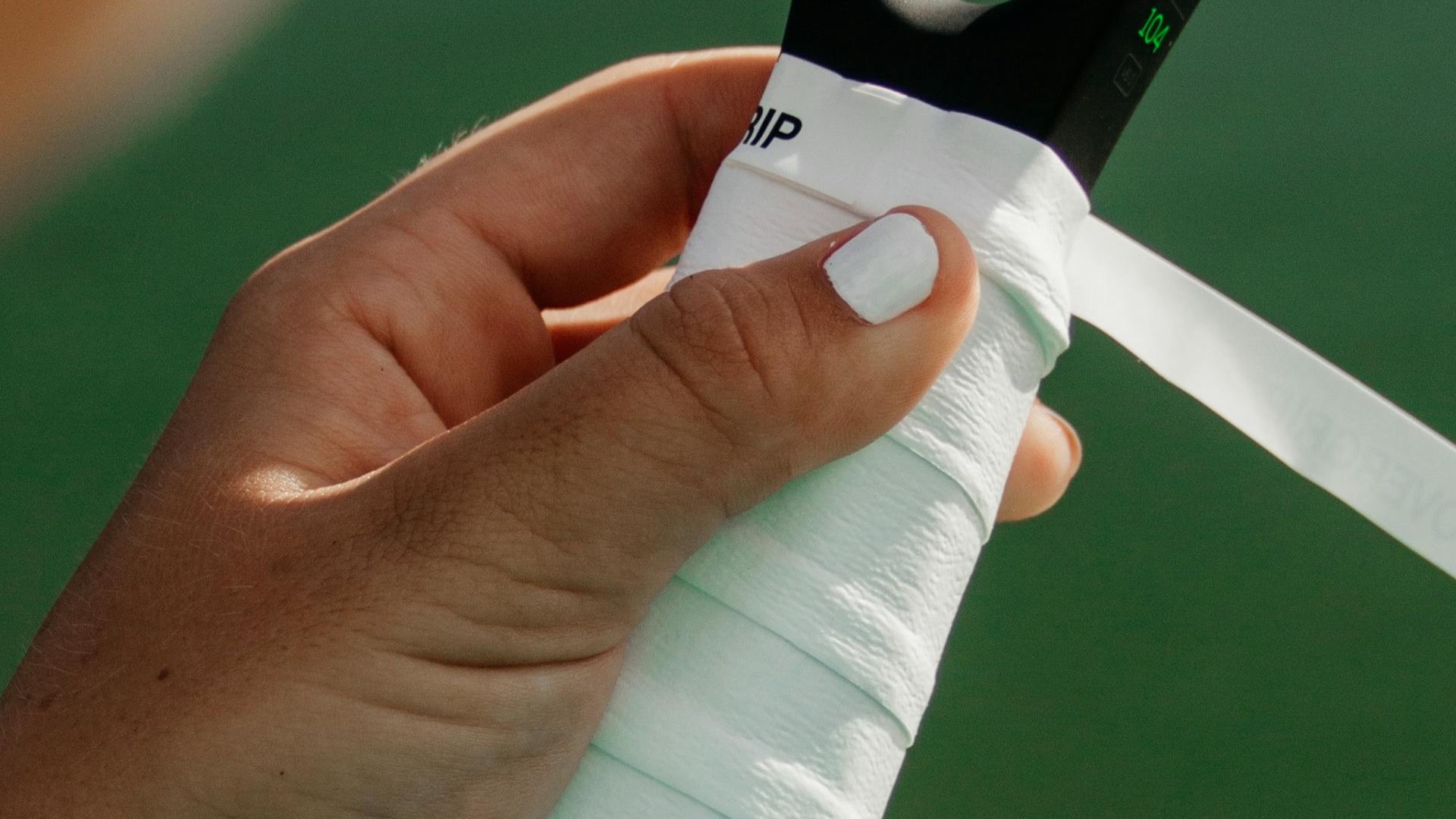 A woman wraps white grip tape around her racquet handle.