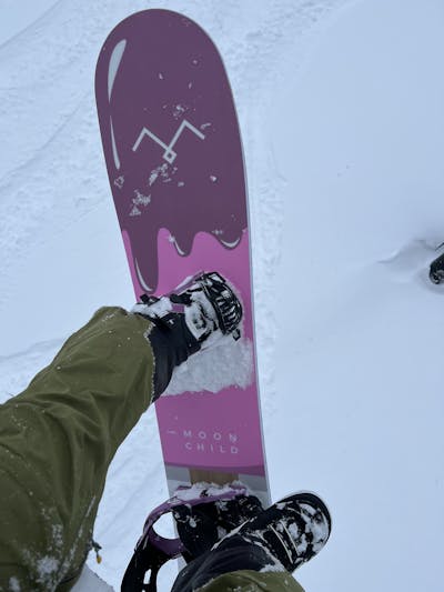 Top down view of a snowboard with bindings attached to someone on a ski lift. 