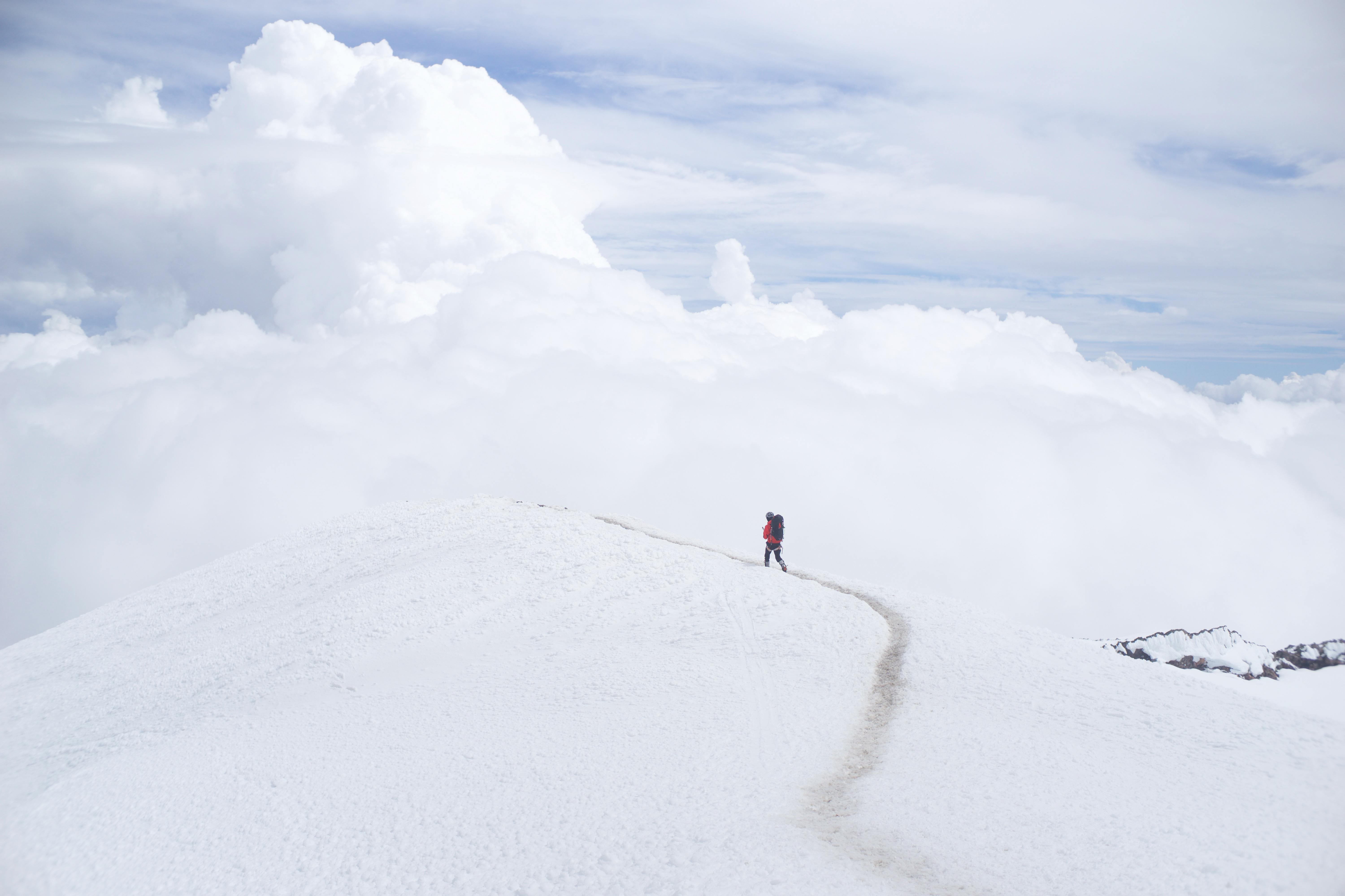 A hiker walking on a trail that winds over a snow-covered mountain ridge