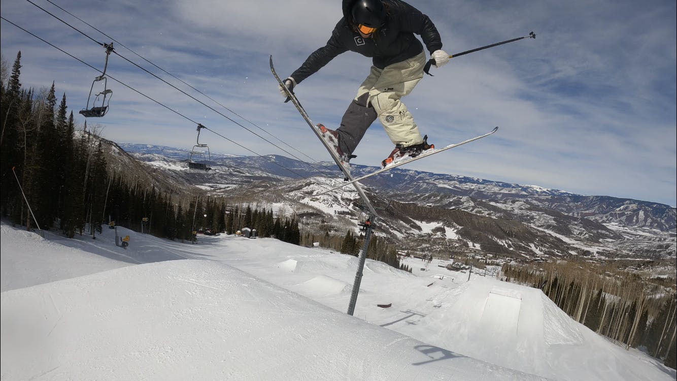 A skier hits a rail. There is a chairlift in the background.
