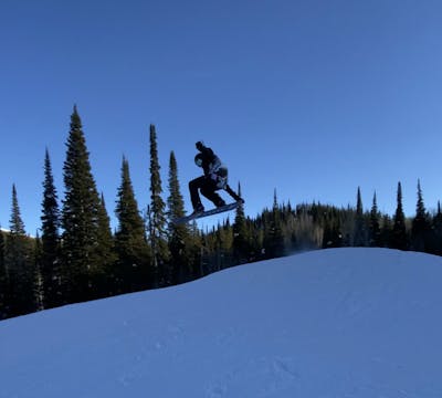 A snowboarder going off of a 30 foot jump on the 2022 Arbor Shiloh snowboard.