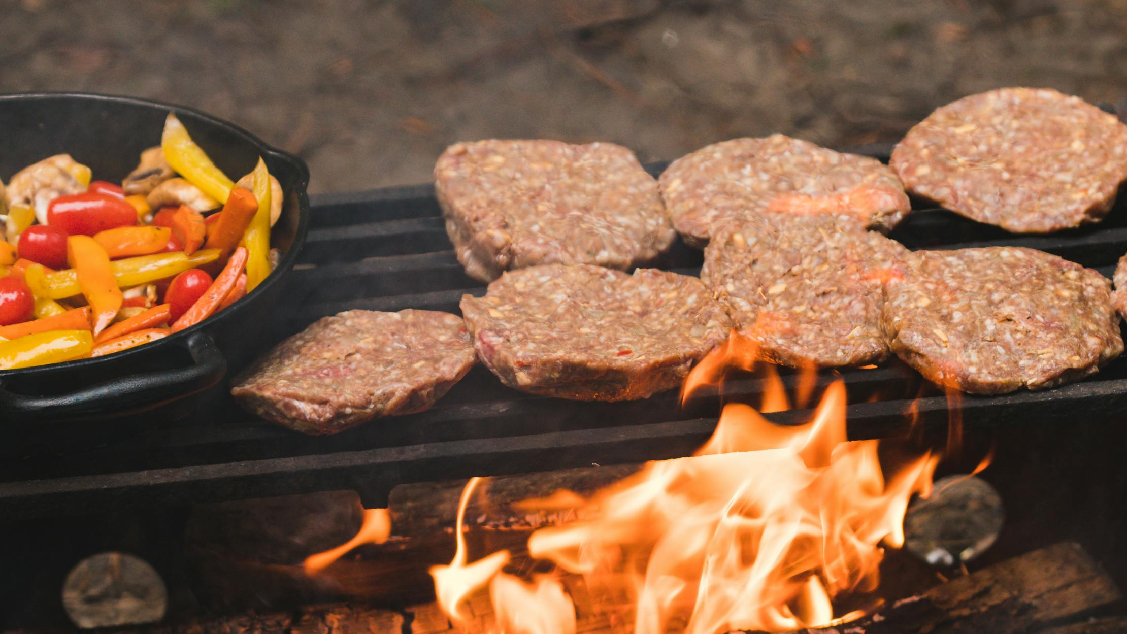 Burger patties and a frying pan grilling vegetables cooking over a campfire