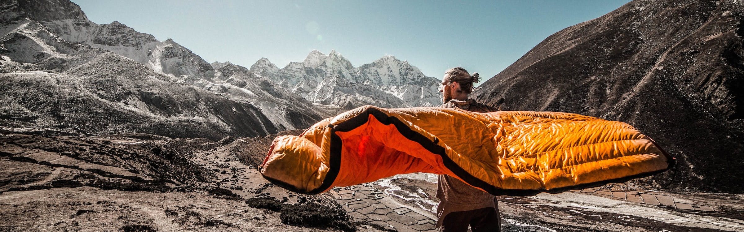 A man holding his sleeping bag out in the wind. 