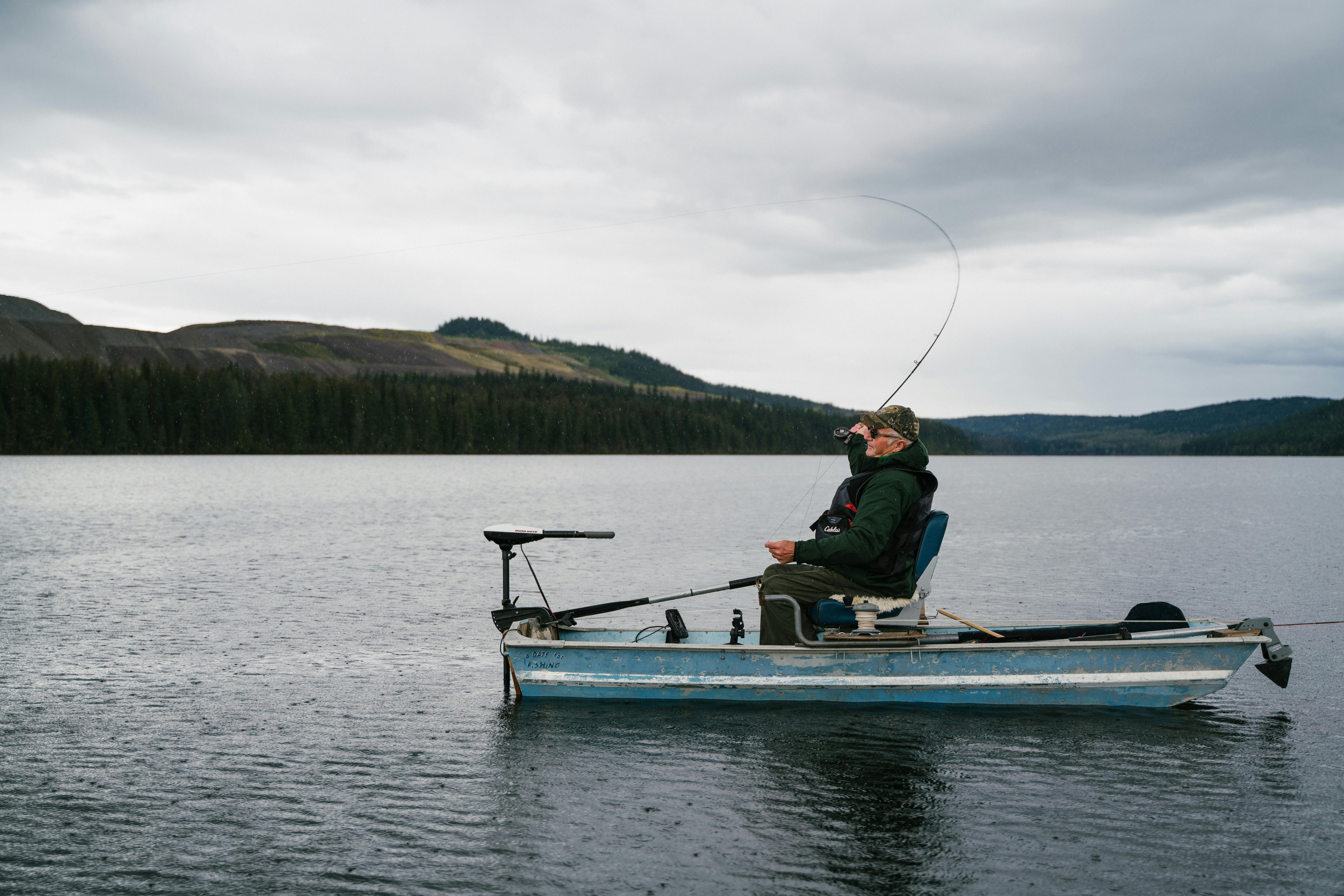 A man fishing from a small boat in a lake. 