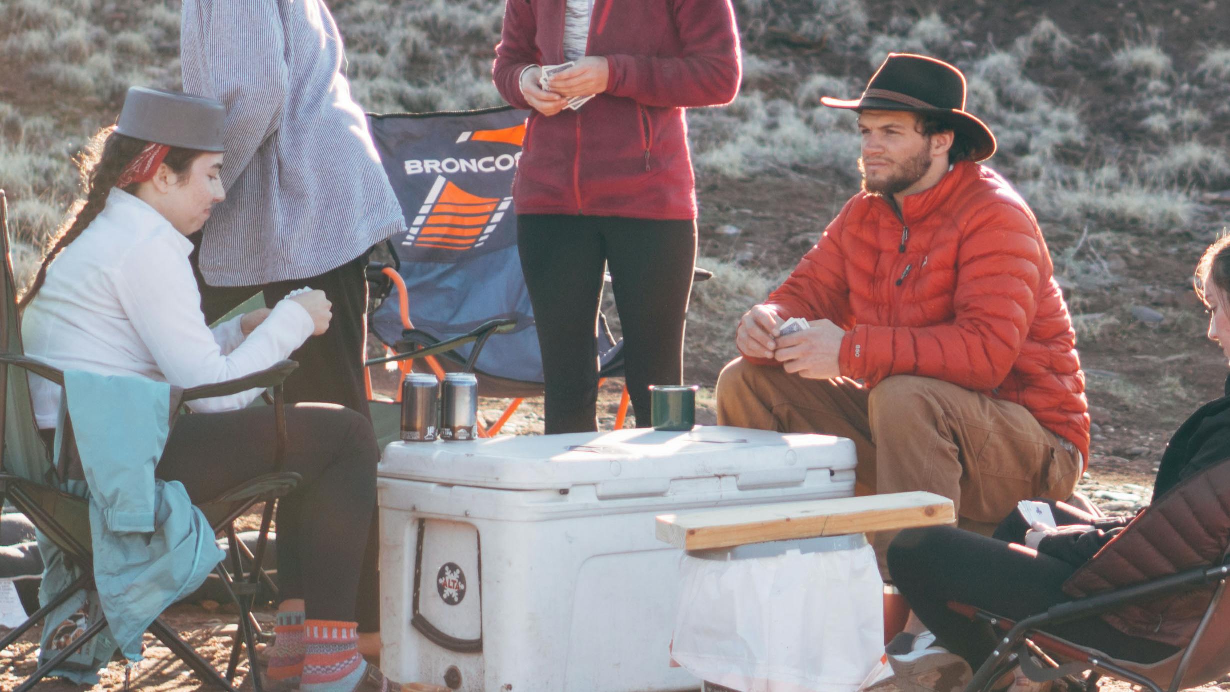 Five people sitting around a cooler while camping.