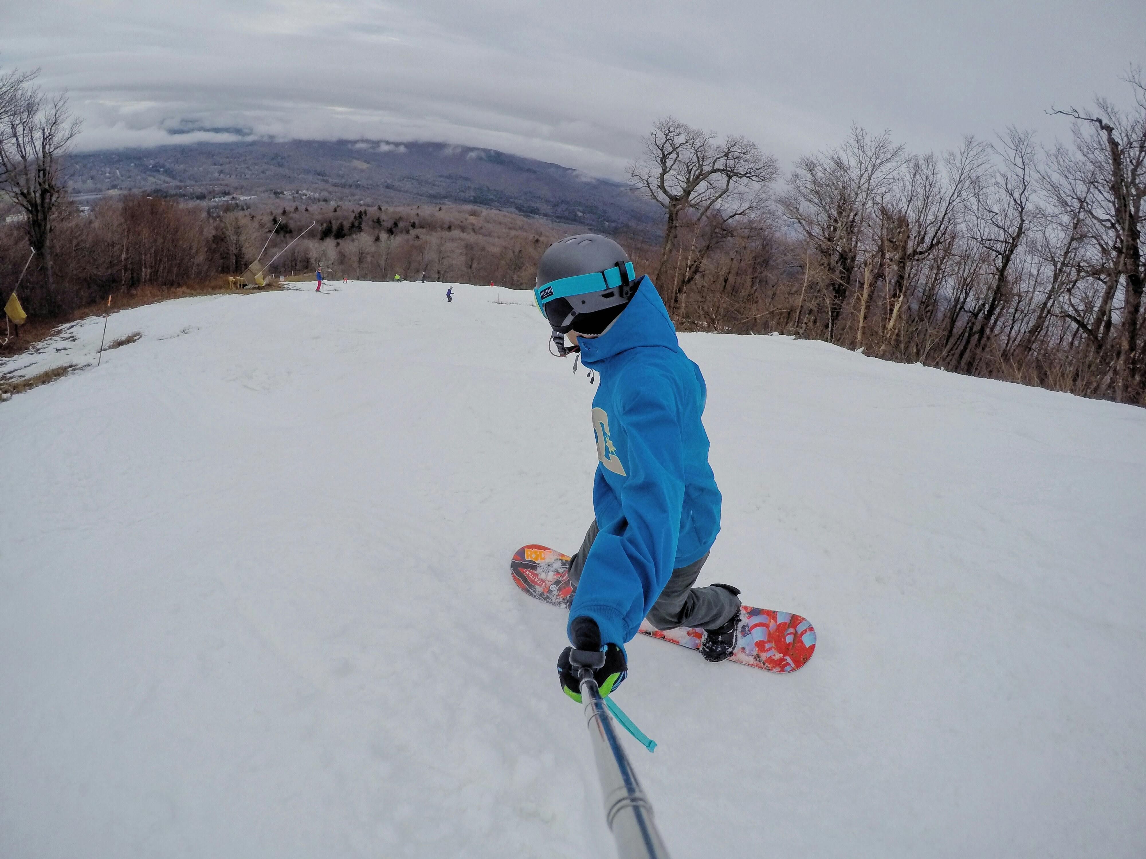 A go pro selfie of a snowboarder turning down a mountain. 