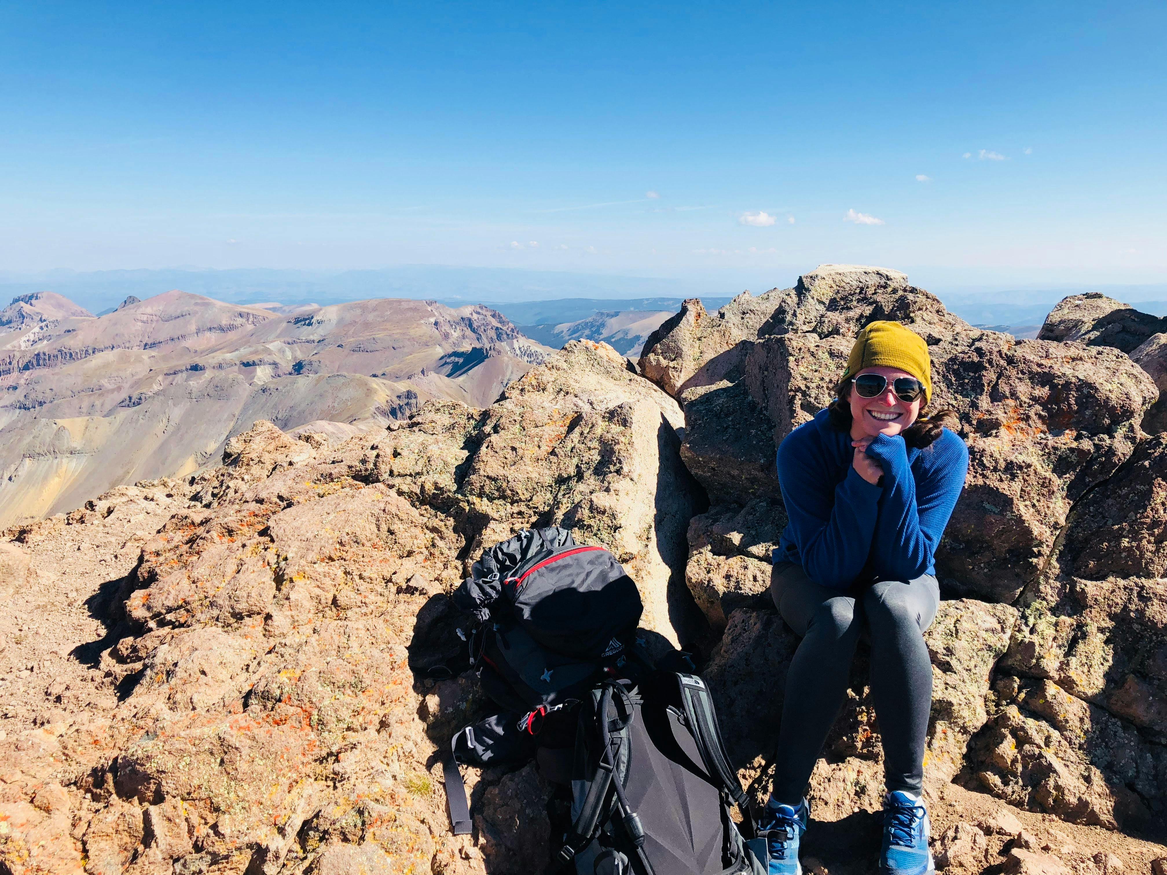 Curated expert Olivia Whitehead sitting on a rocky summit with her backpack