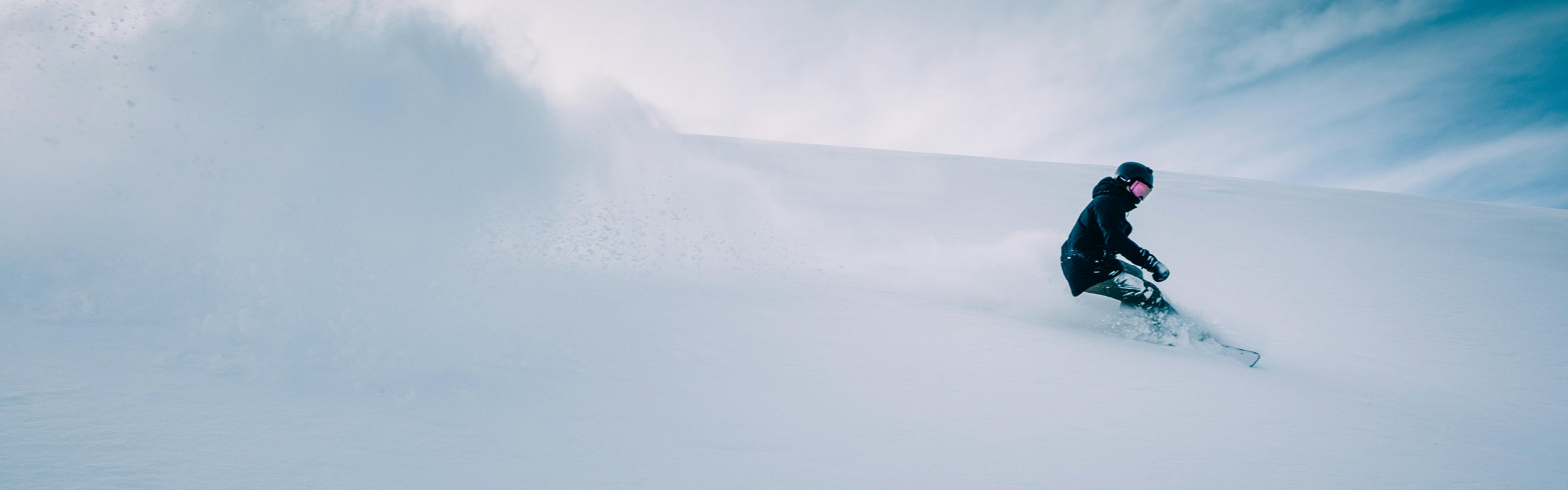 A snowboarder turning down a snowy hill. 