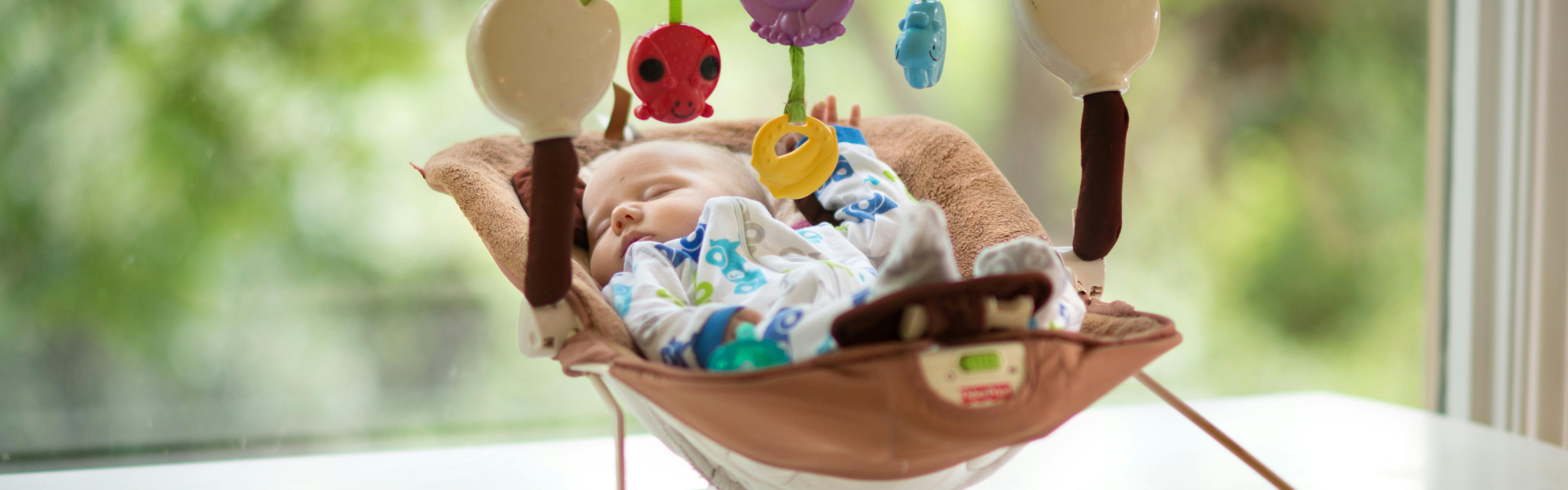 A baby sleeping in a bouncer.