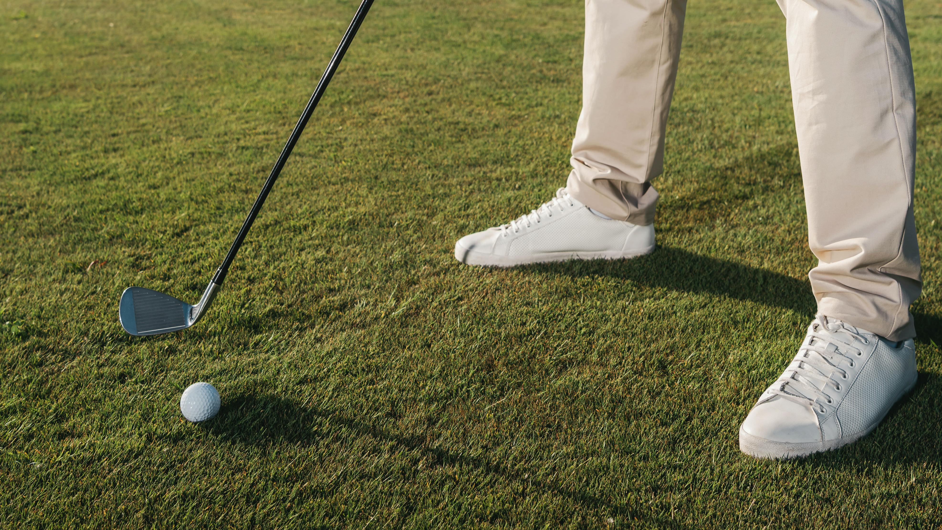 A golfers feet as he sets up to hit a ball with an iron. 
