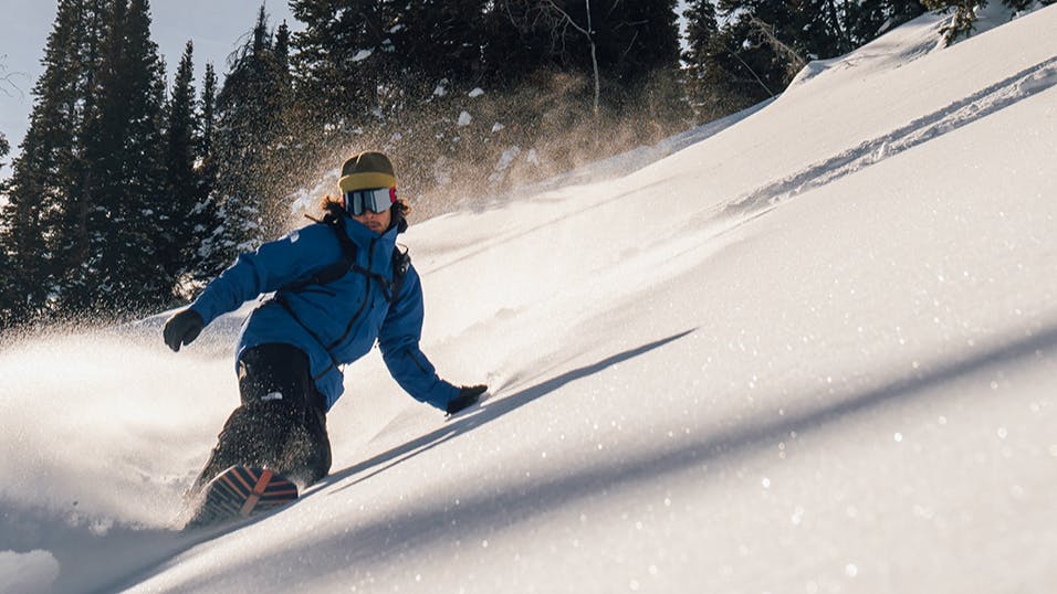 An Arbor athlete snowboards down a steep hill, carving into the mountain and sending up a spray of powder. 