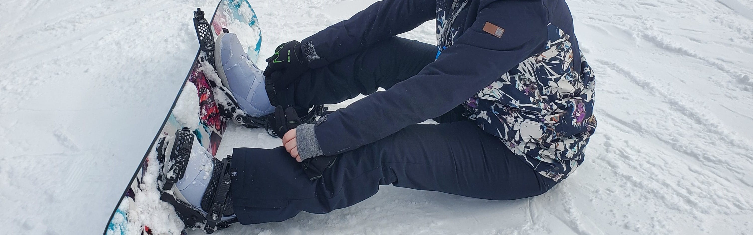 A snowboarder sitting in the snow in the Roxy Women's Backyard Pants.