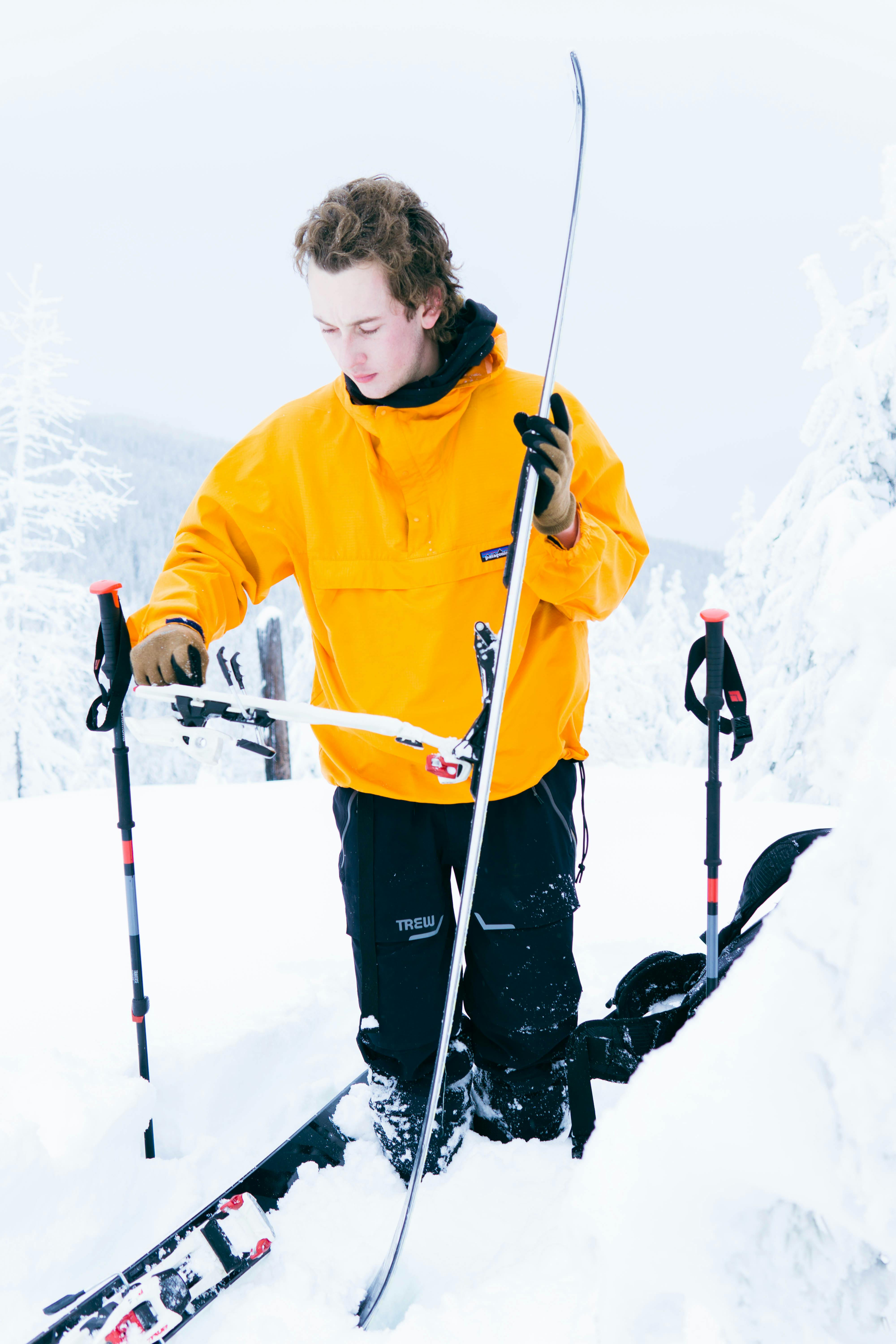 A man in a yellow jacket gets his skis set up while standing deep in the snow.
