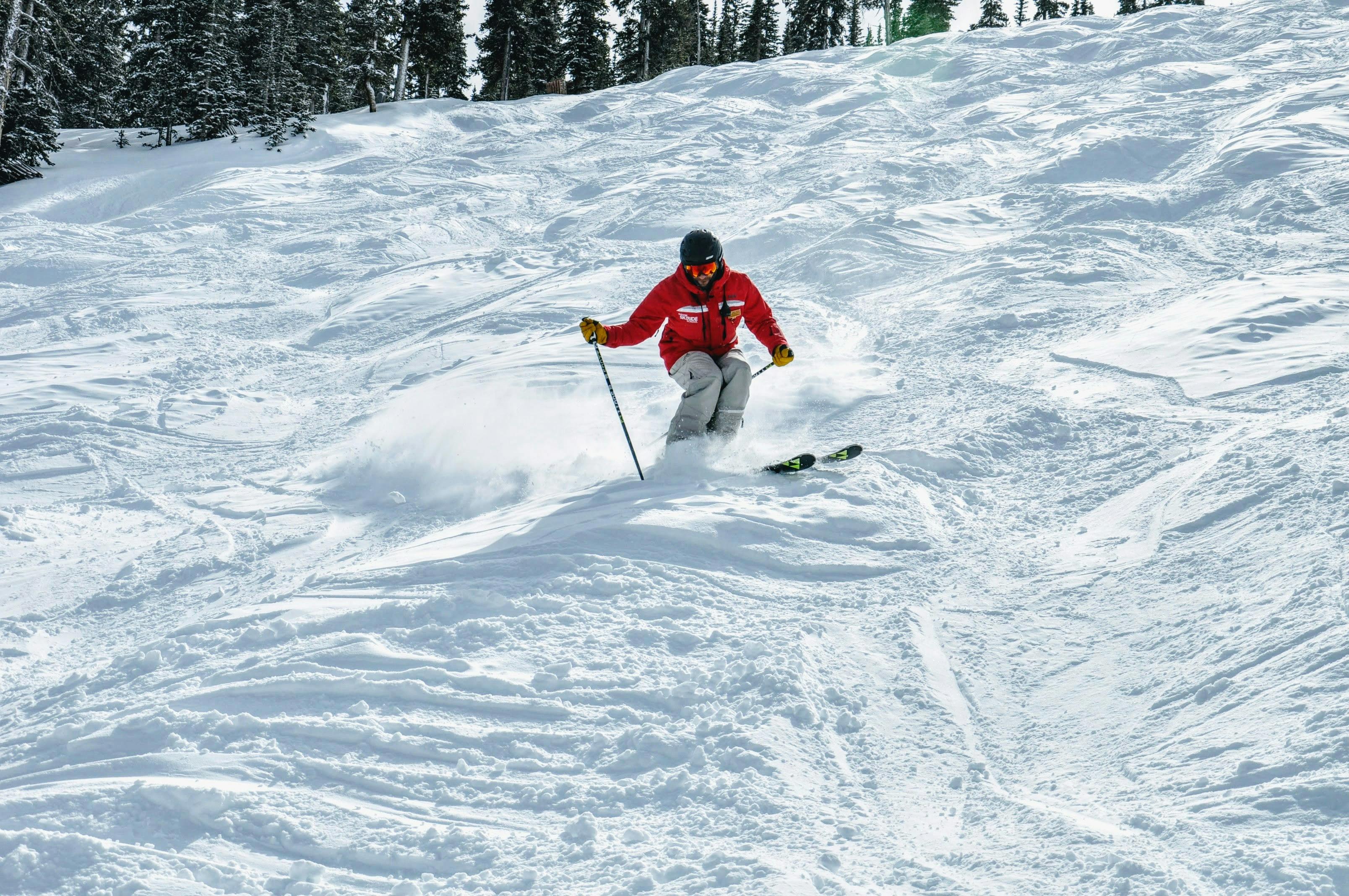 A skier in a red jacket heading down a mogul field