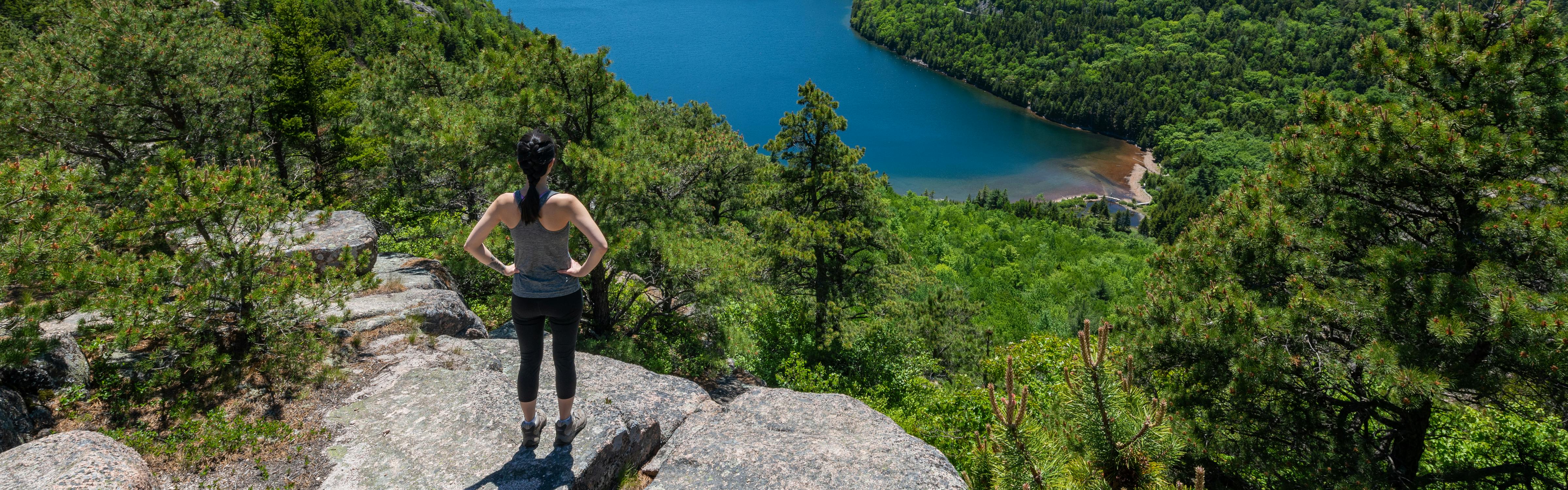 Woman standing on a cliff, looking out at the forest and lake below