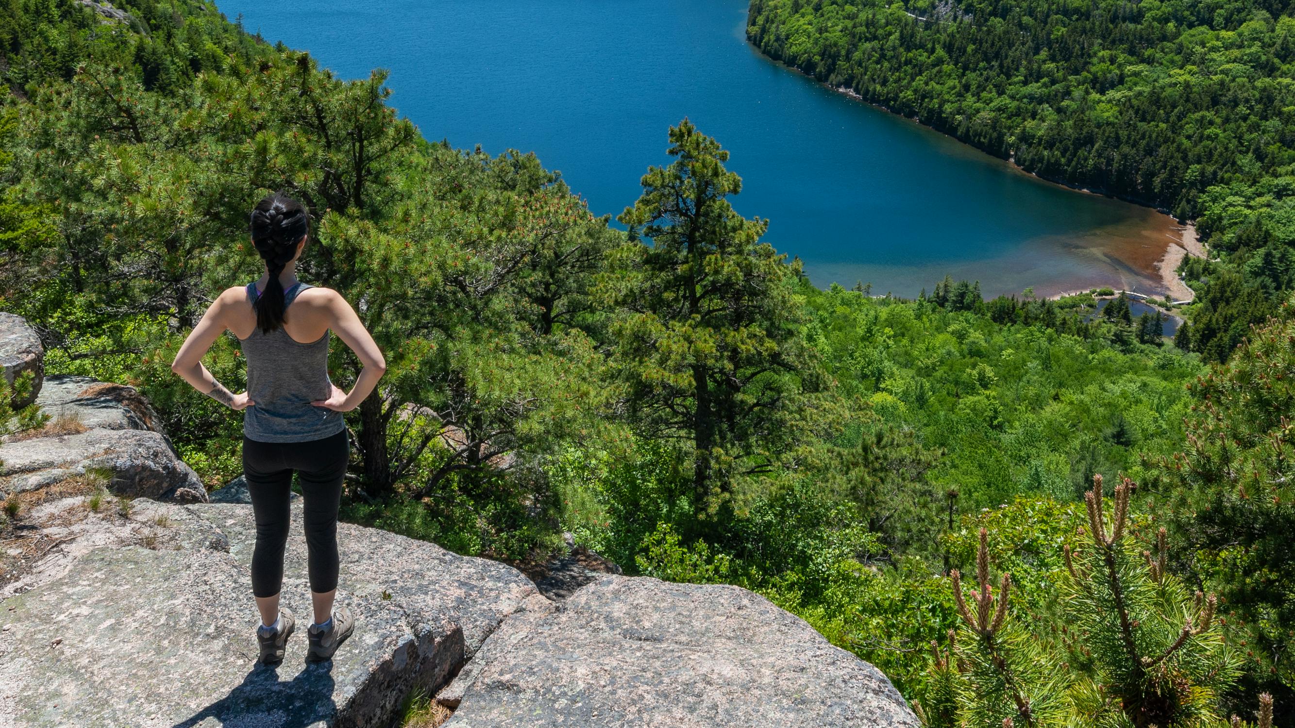 Woman standing on a cliff, looking out at the forest and lake below