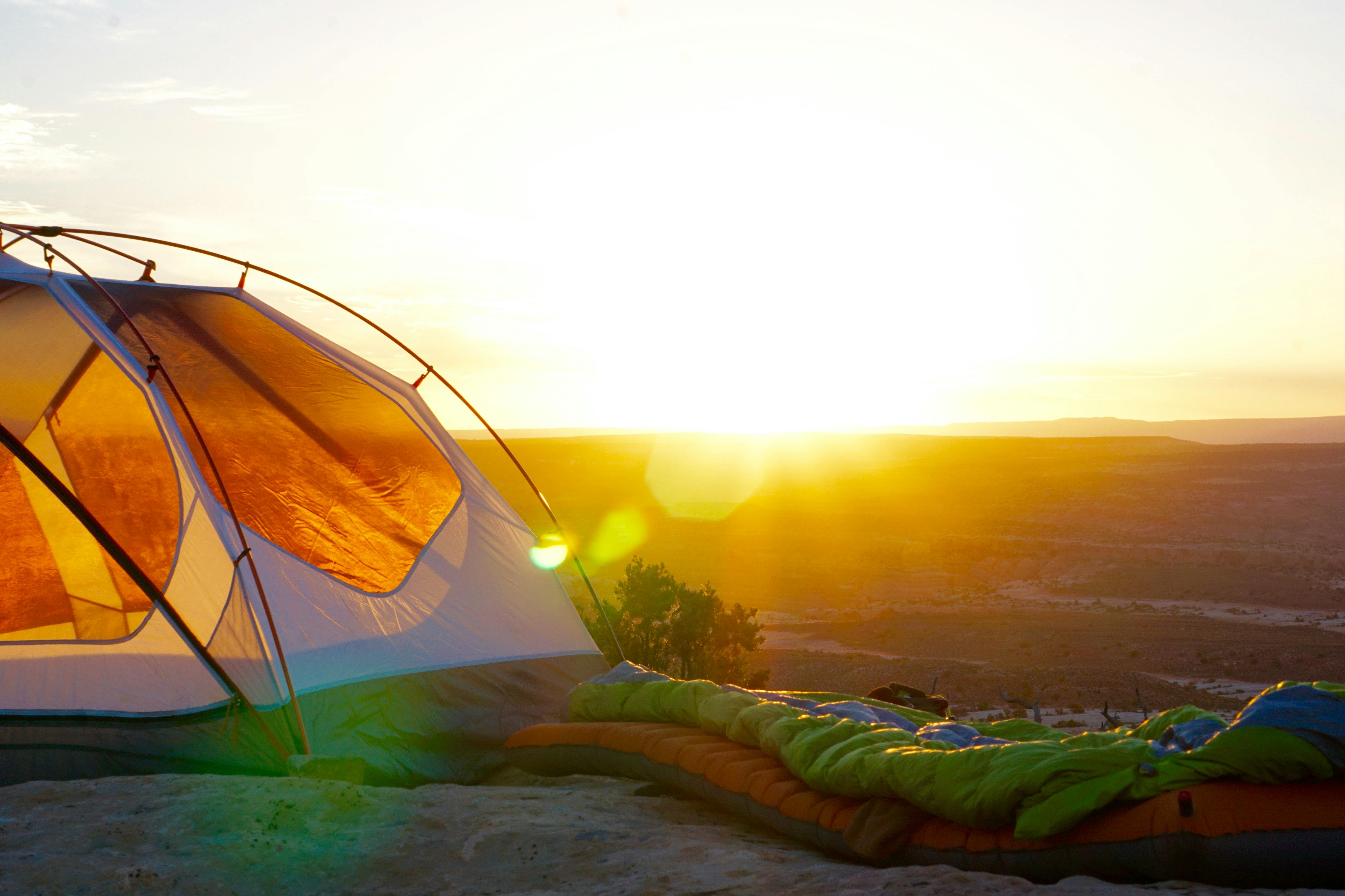 A sleeping bag next to a tent on an overlook with the sun setting in the background
